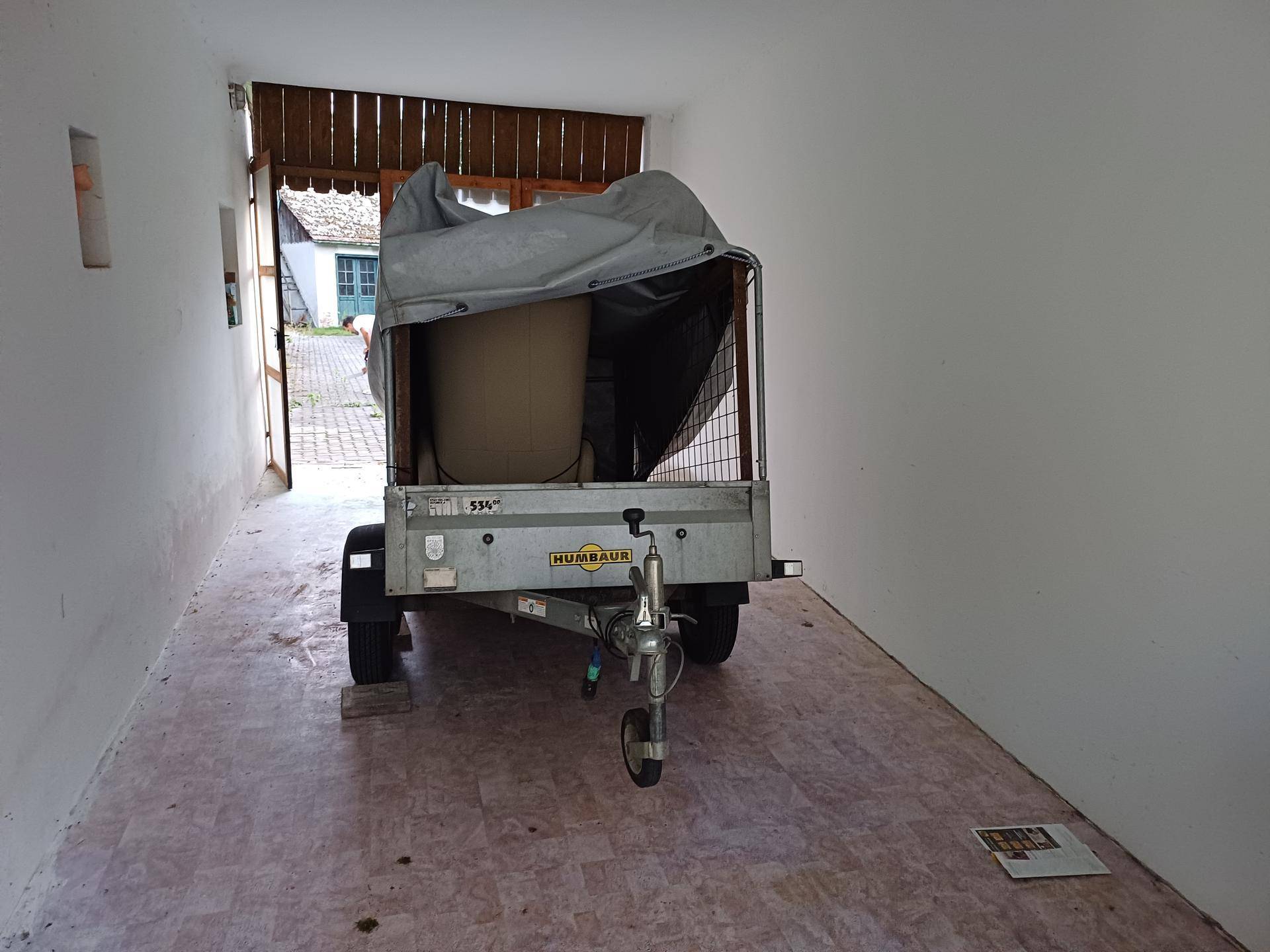 Innenansicht einer Garage mit einem abgestellten Anhänger und Blick nach draußen.