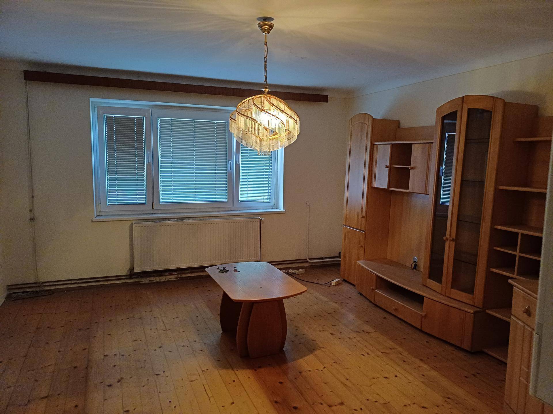 Wohnzimmer mit Holzdielenboden, älteren Holzmöbeln und einem Fenster mit Jalousien.