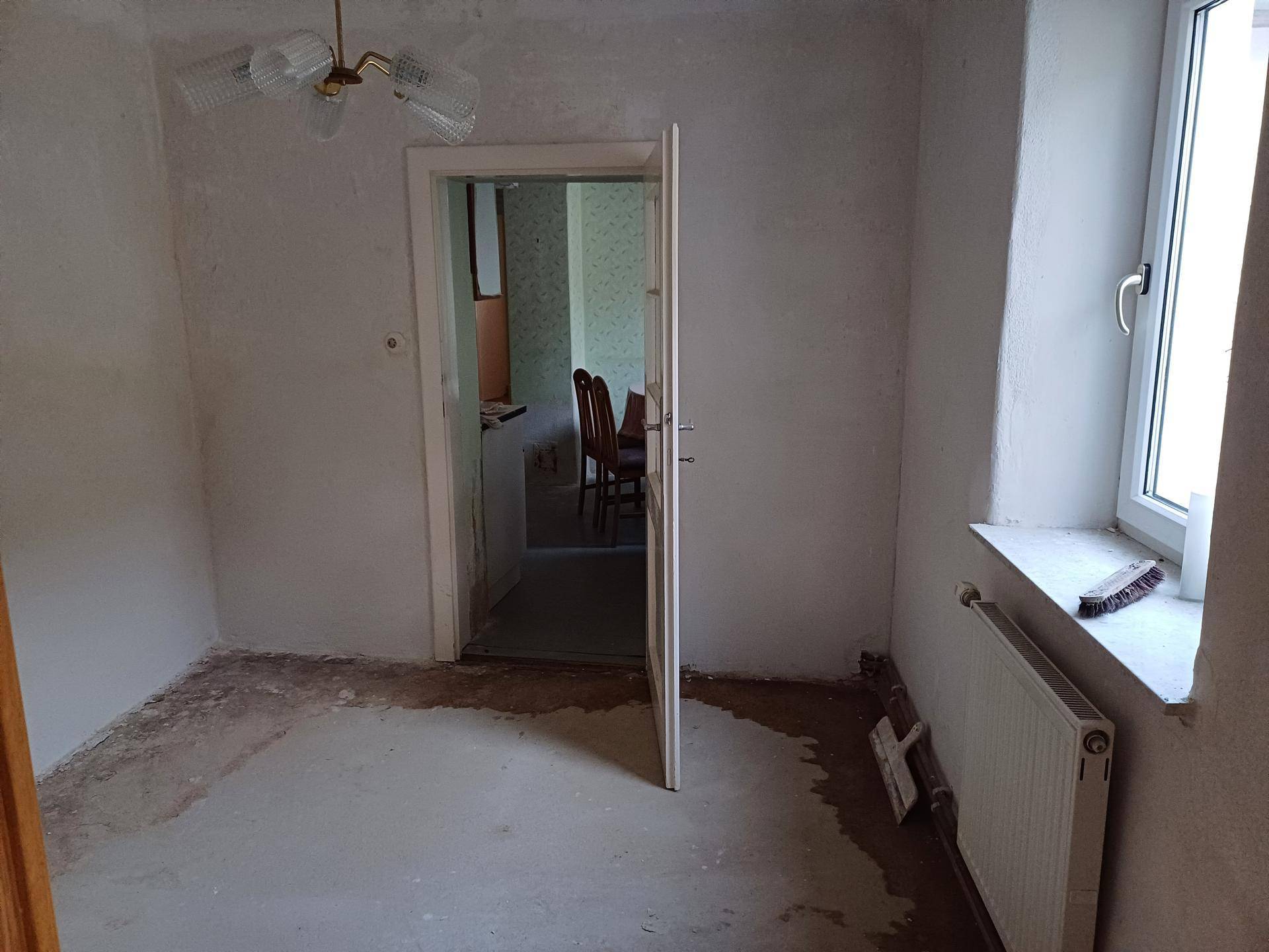 Leerer Raum mit unfertigem Boden, einem Fenster und Heizkörper, bereit zur Renovierung.