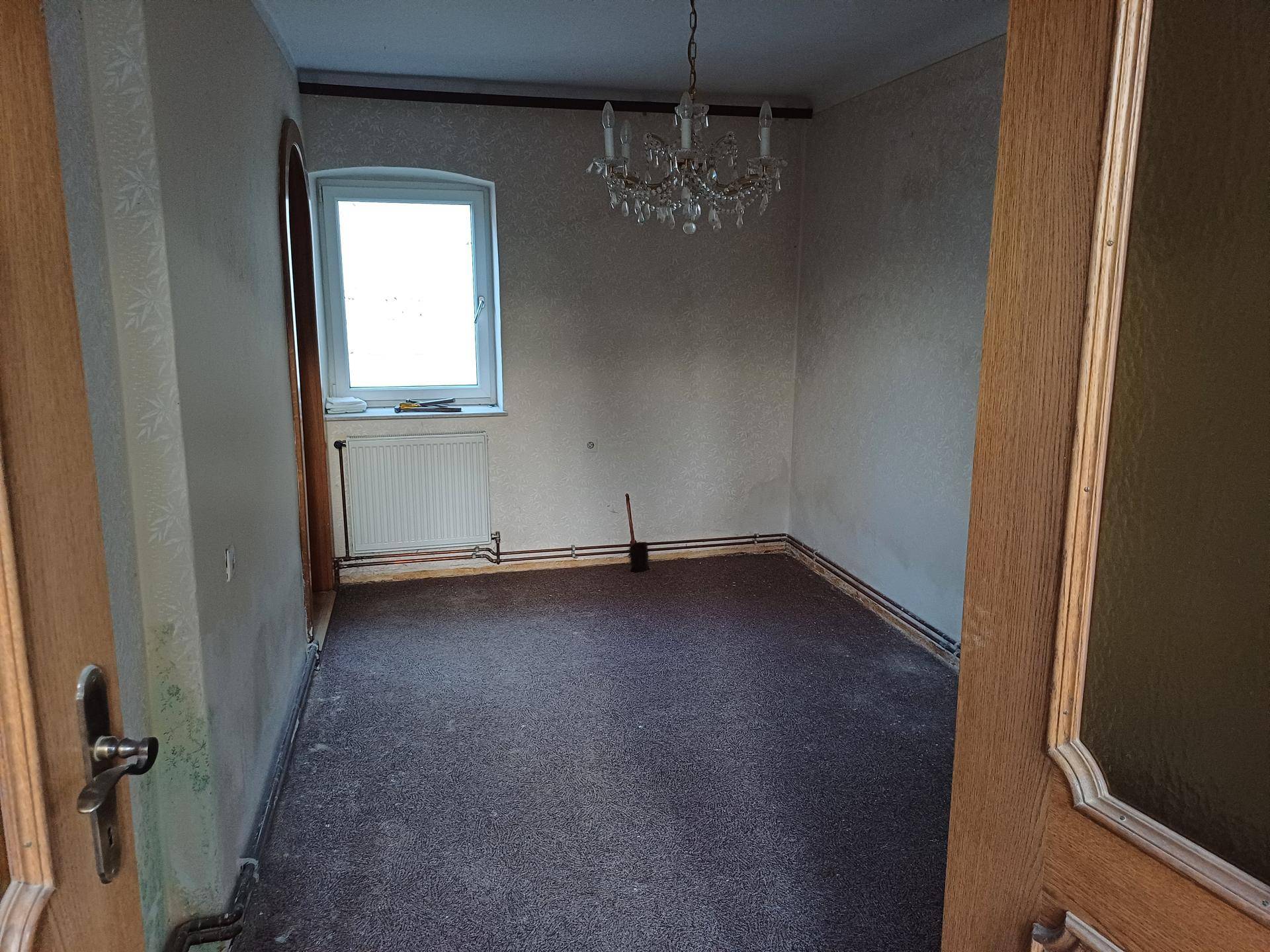 Leerer Raum mit Teppichboden, einem Fenster und einem Kronleuchter an der Decke.