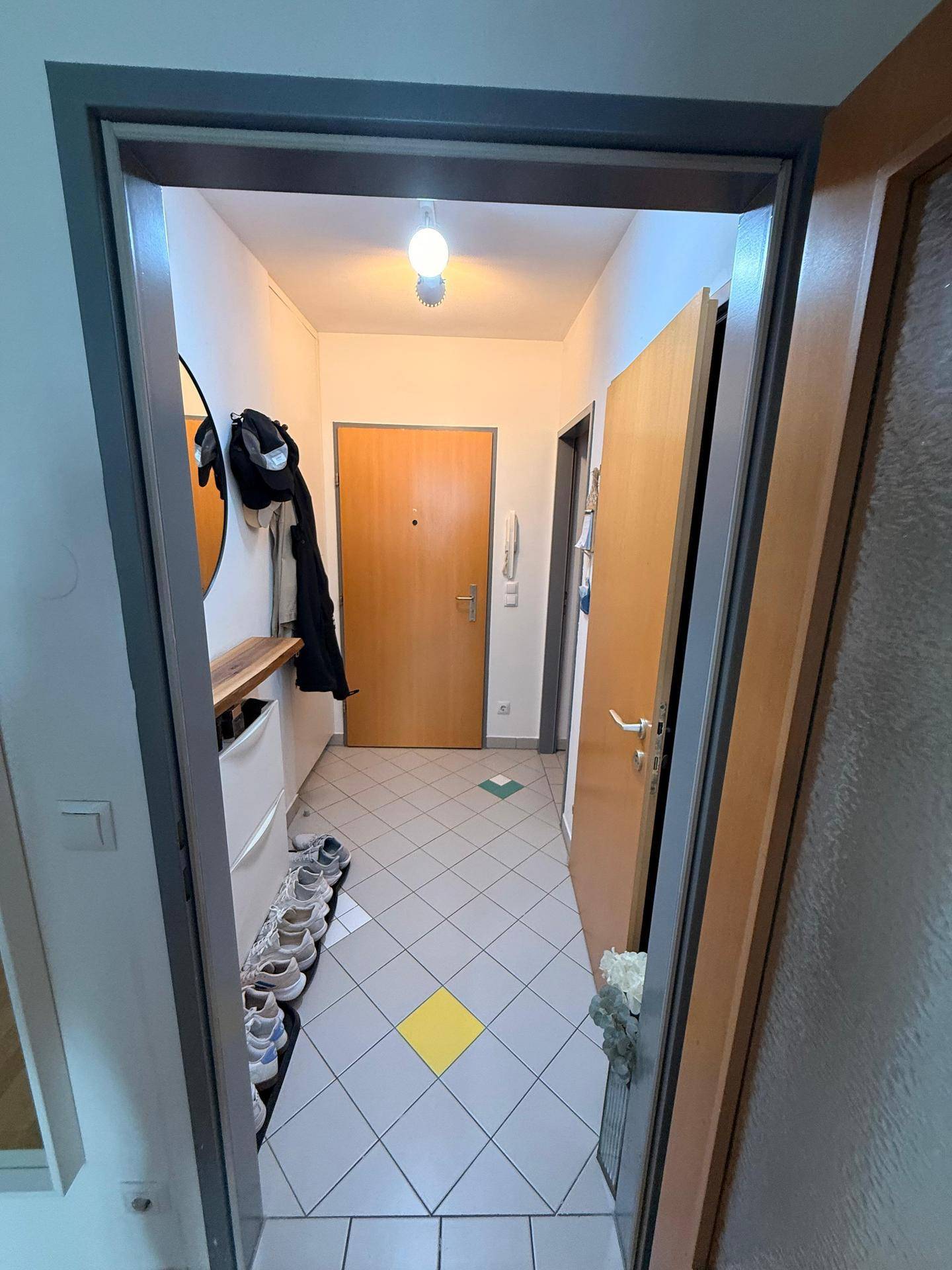 Eingangsbereich mit Fliesenboden, praktischem Schuhschrank und runden Spiegel, funktional eingerichtet.