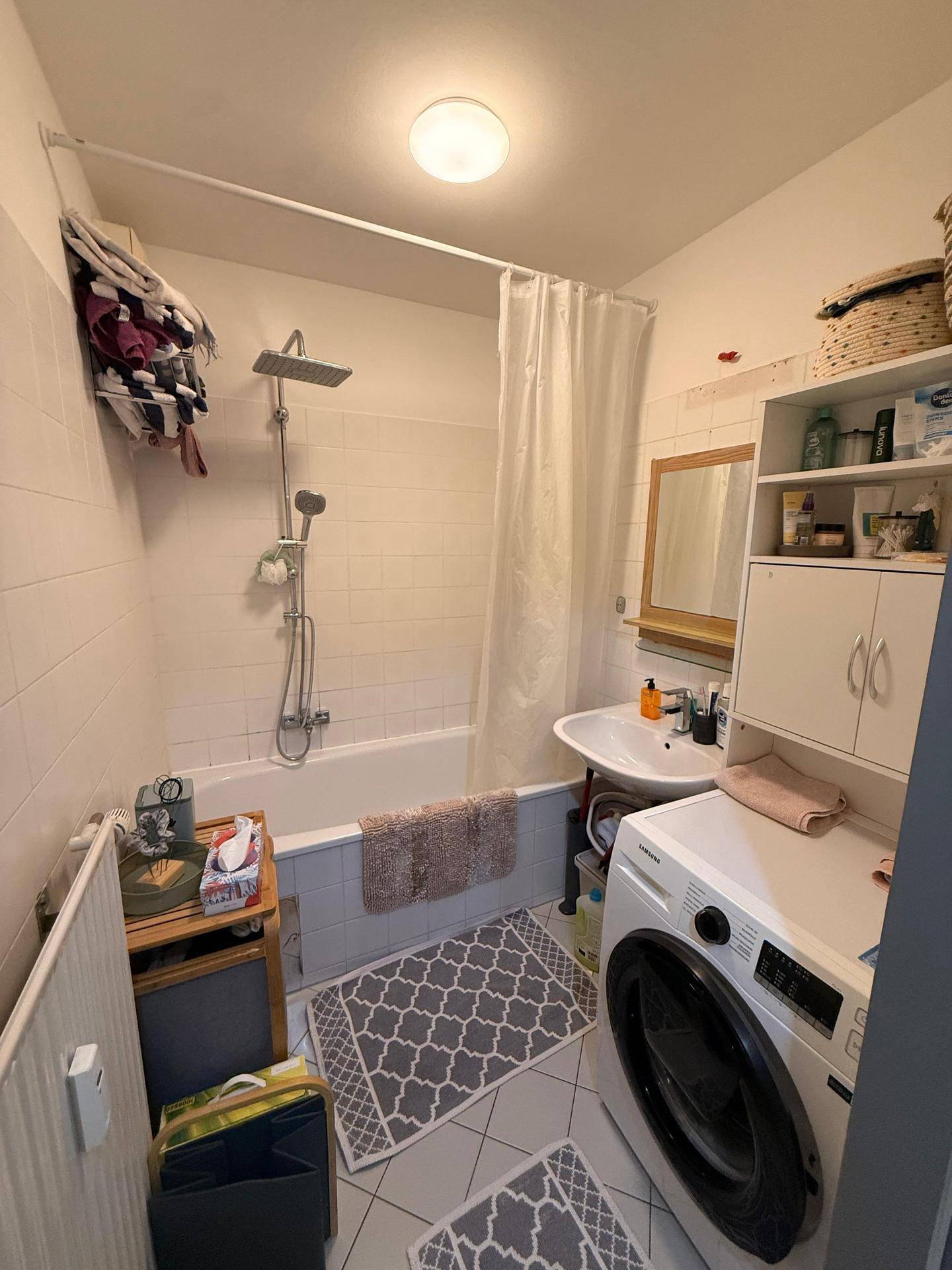 Badezimmer mit Badewanne, Duschvorrichtung, Waschbecken und integrierter Waschmaschine.