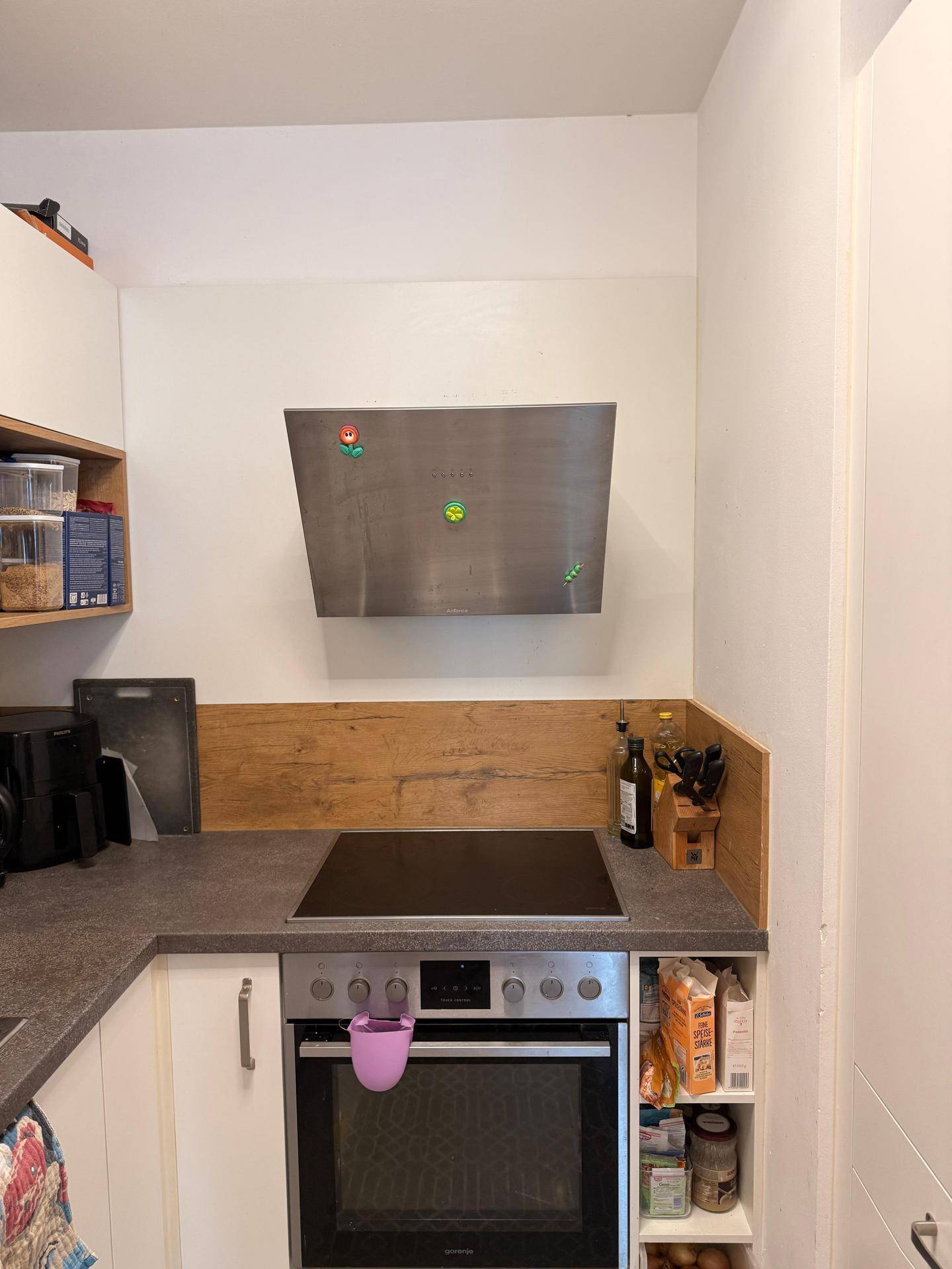 Kochbereich mit Cerankochfeld, Backofen und Dunstabzugshaube, umgeben von Holzrückwand.