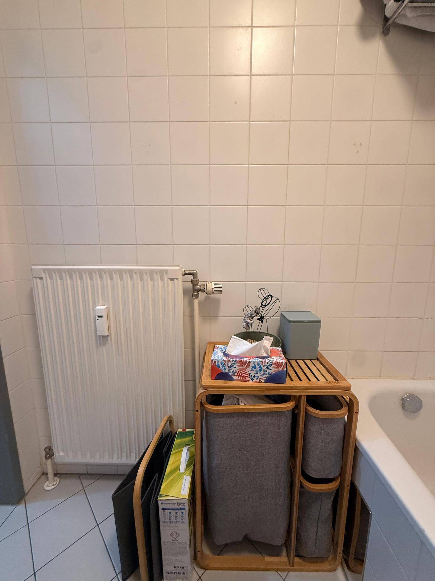 Heizkörper und kleiner Holzschrank neben der Badewanne, bietet zusätzlichen Stauraum.
