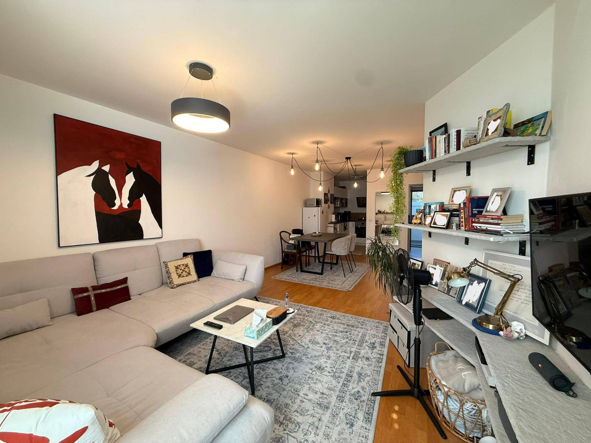 Geräumiger Wohnbereich mit beigem Ecksofa, modernen Kunstwerken und Blick auf den Essbereich.