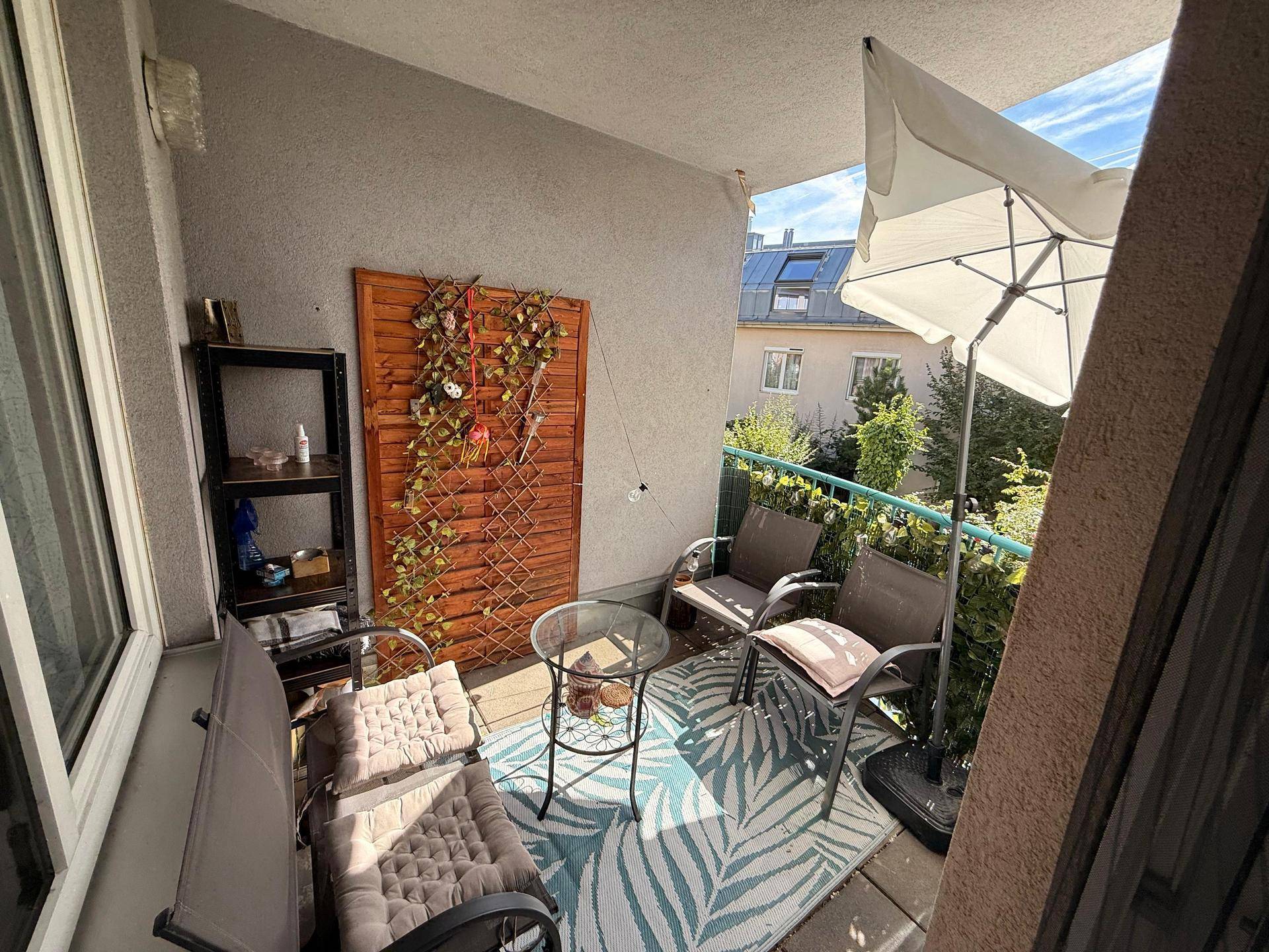 Gemütlicher Balkon mit Sitzgelegenheiten, Sonnenschirm und Blick ins Grüne.