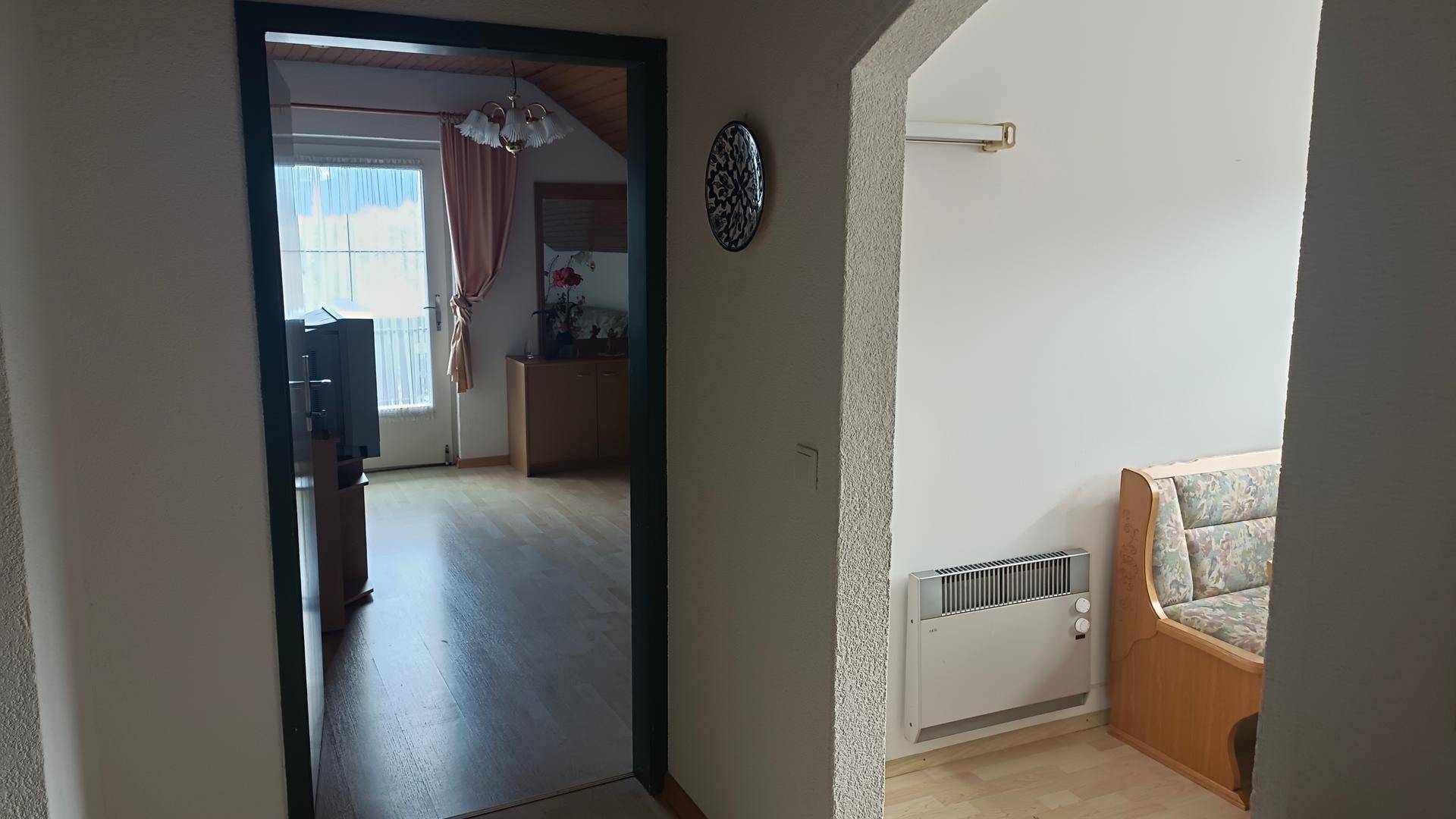 Flur mit Heizkörper und Blick in einen angrenzenden Raum mit Holzboden.