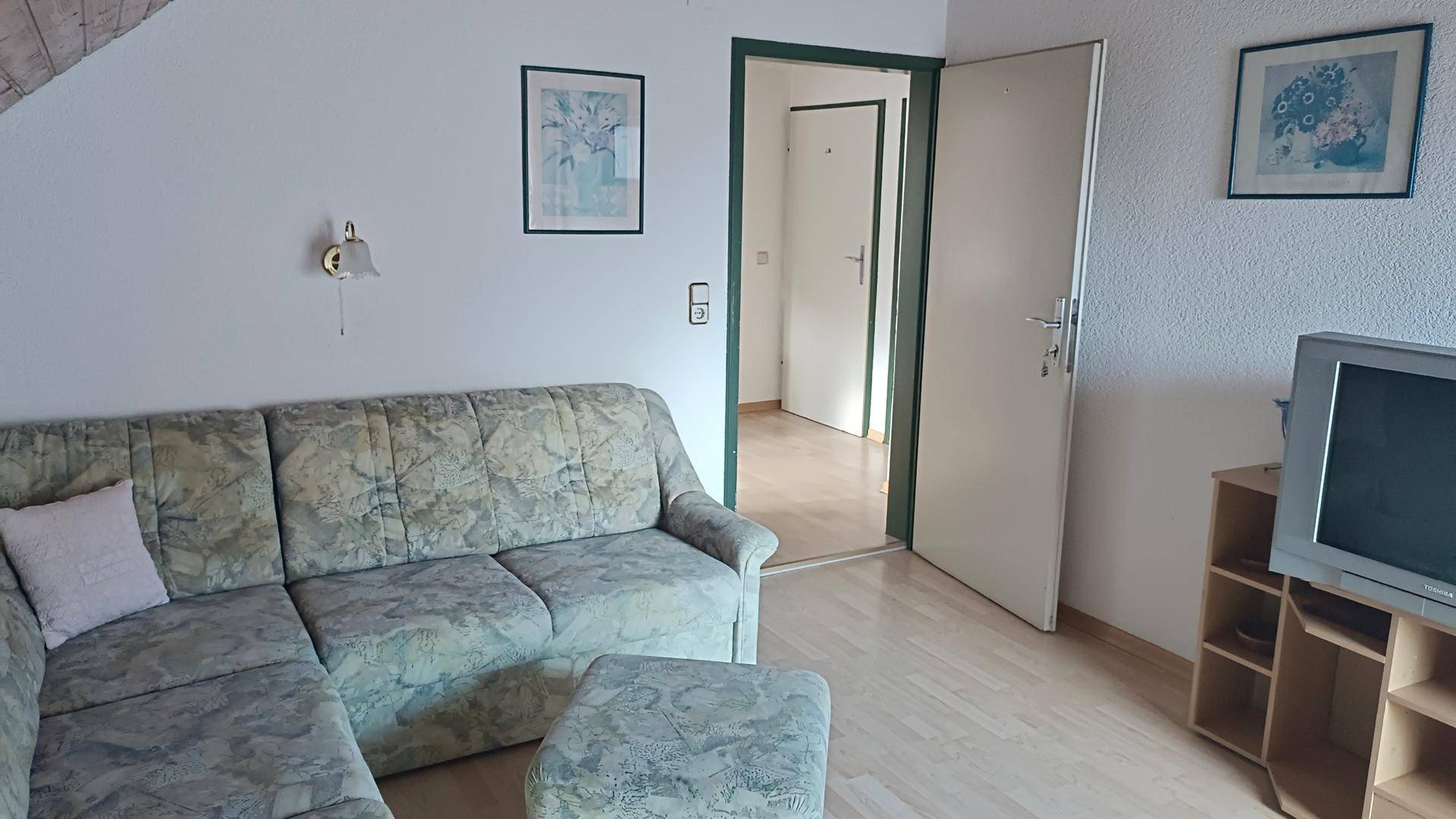 Wohnzimmer im Dachgeschoss mit Sofa, Fernseher und Blick auf eine Tür.
