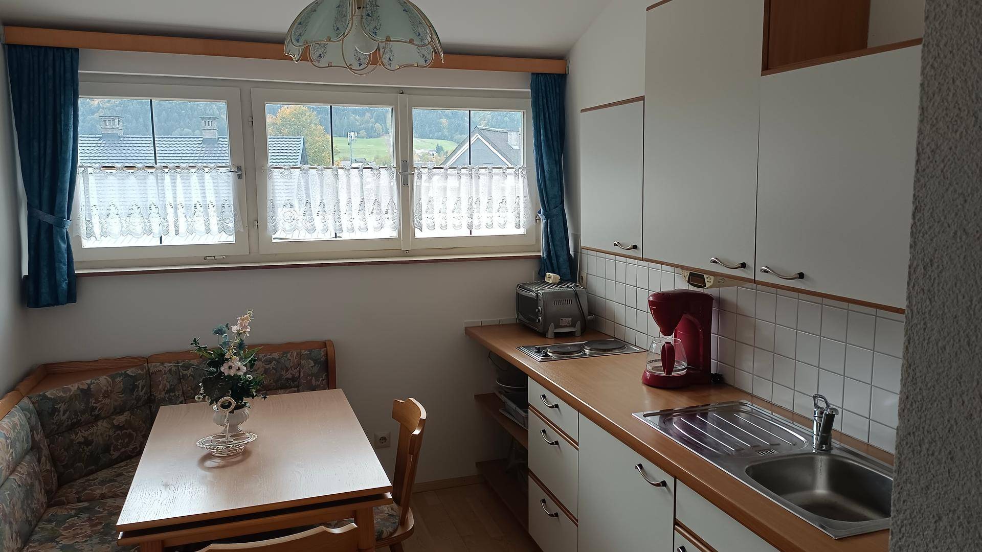 Kleine Küche mit weißer Einbauküche, Esstisch und Fenster mit Bergblick.