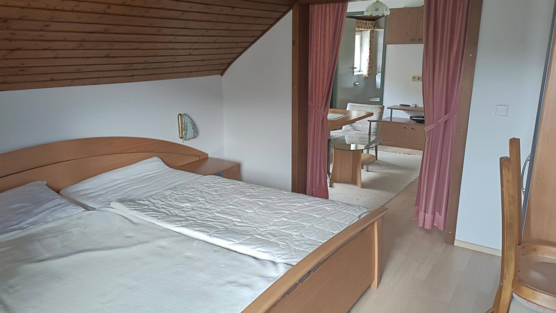 Schlafzimmer mit Doppelbett, Dachschräge und Zugang zum Wohnbereich.