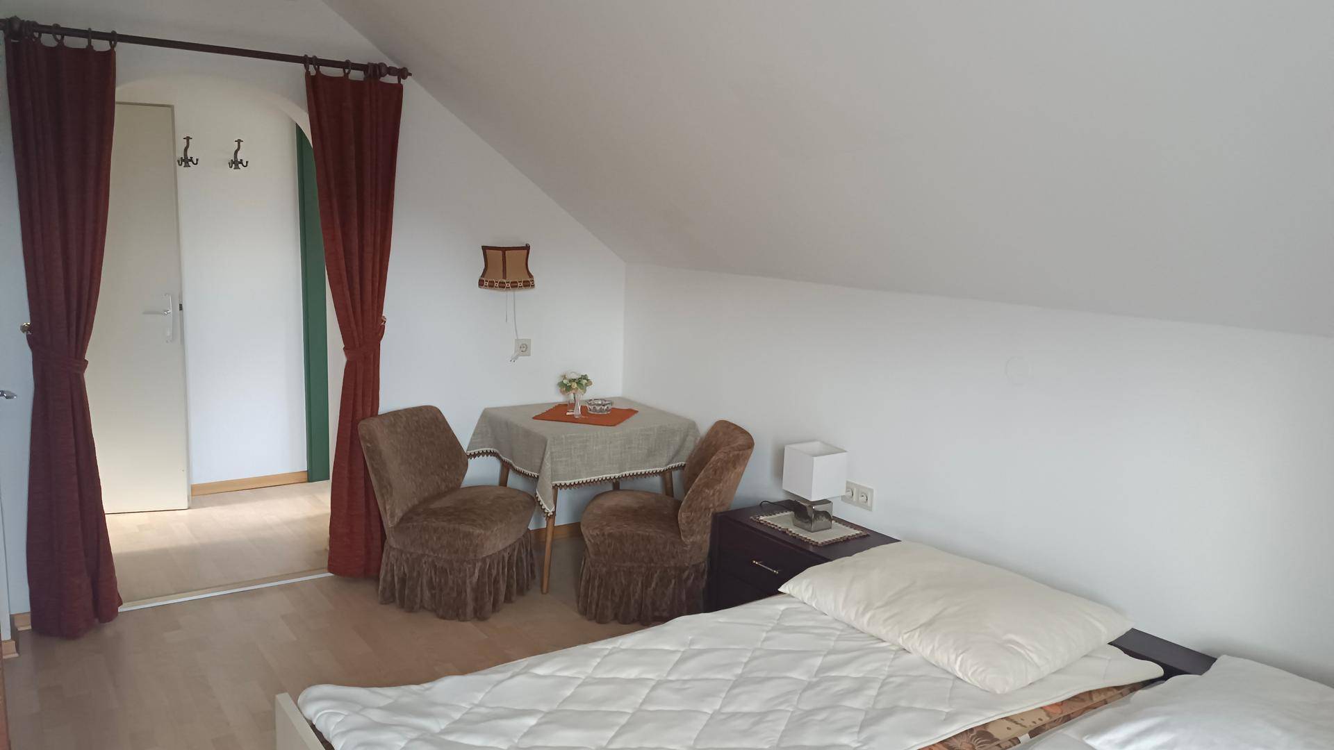 Schlafzimmer im Dachgeschoss mit Einzelbett, kleinem Tisch und schrägen Wänden.