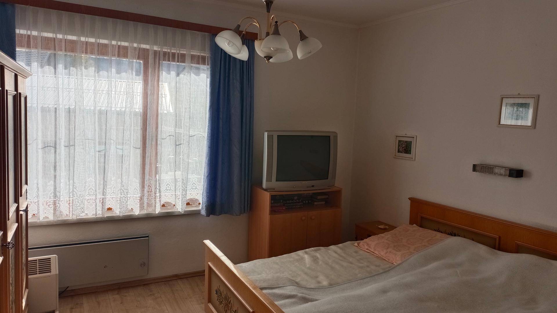 Schlafzimmer mit Holzbett, Heizkörper und Fenster mit Vorhängen.