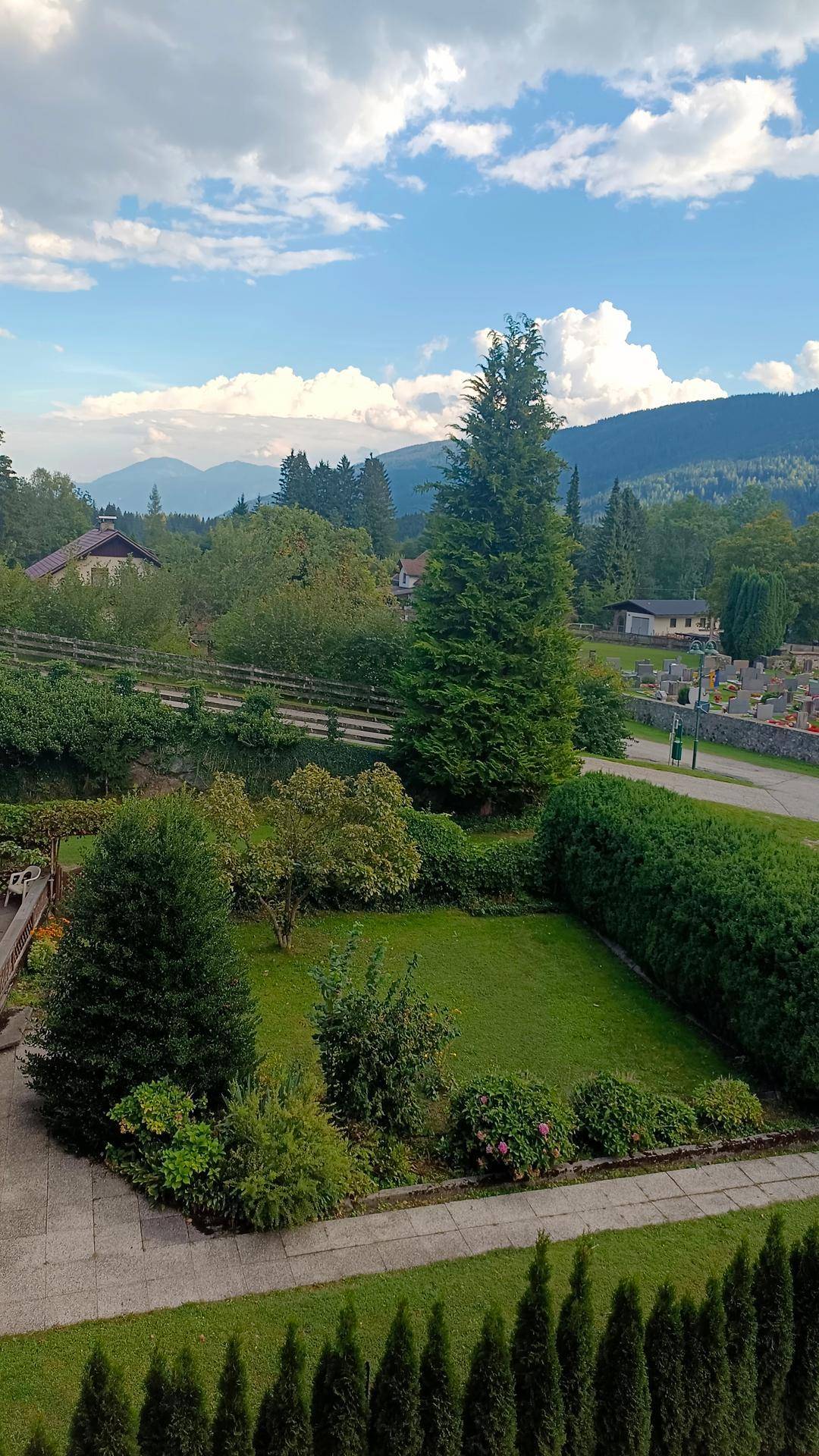 Gepflegter Gartenbereich mit Hecken und Bäumen, umgeben von einer malerischen Berglandschaft.