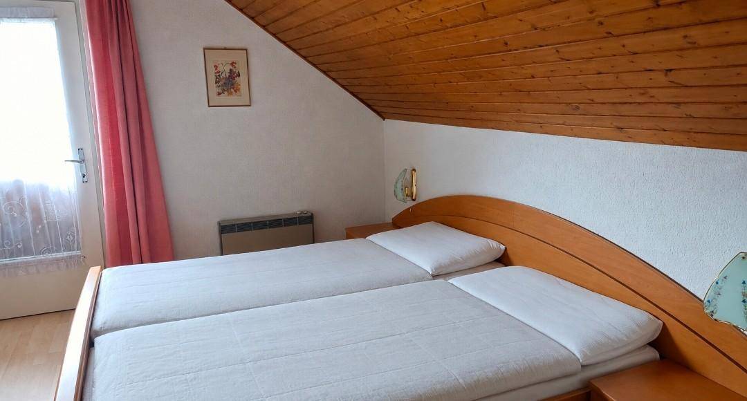 Helles Schlafzimmer im Dachgeschoss mit Holzbalkendecke, zwei Einzelbetten und Zugang zum Balkon.