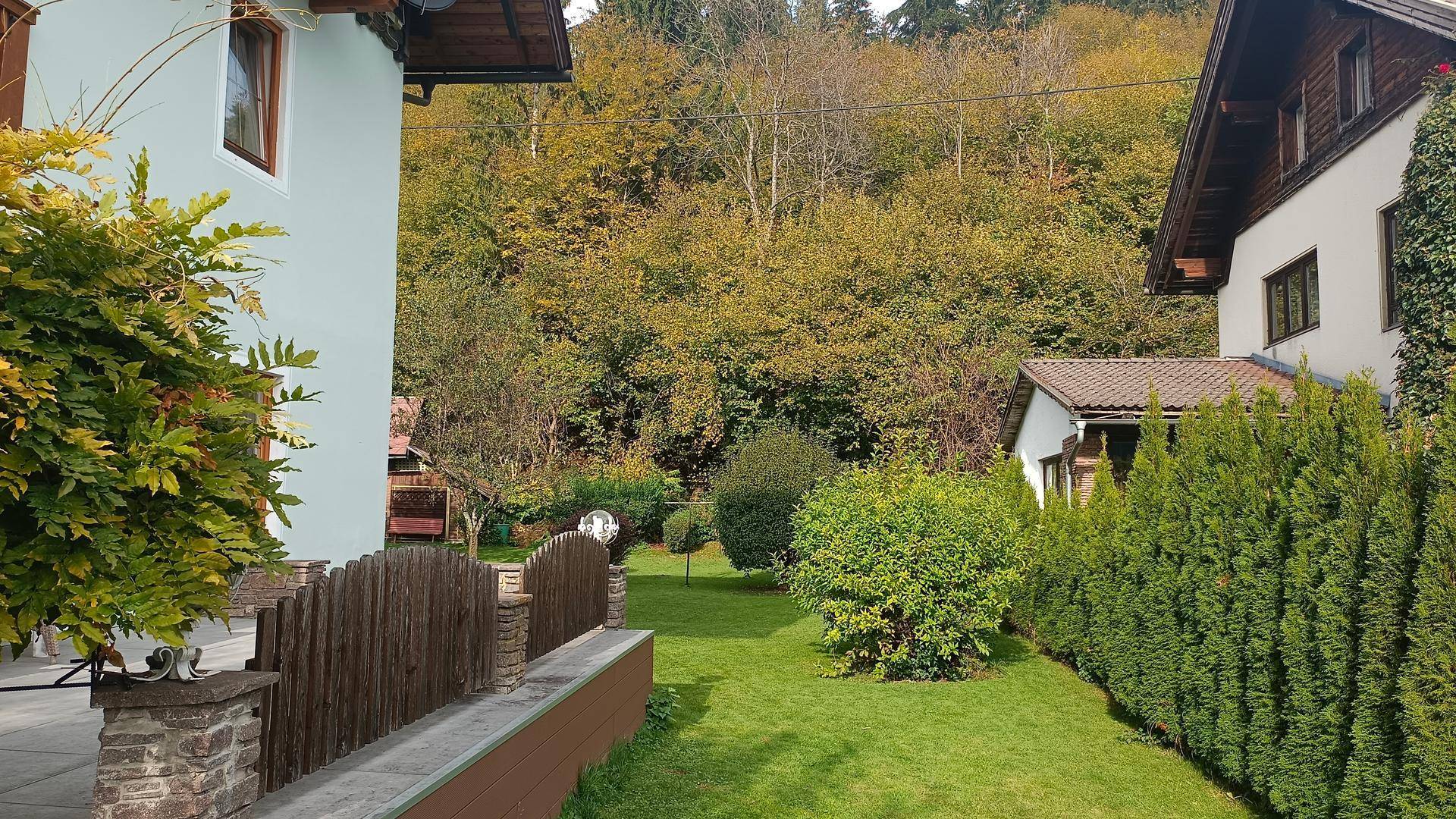 Großer, gepflegter Rasenbereich mit Hecken und Bäumen, umgeben von herbstlicher Waldlandschaft.