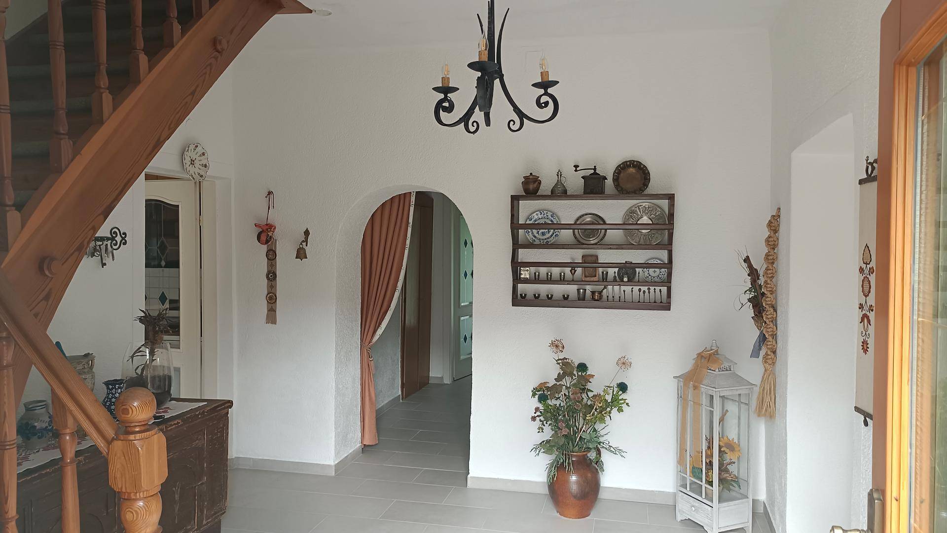 Geräumiger Flur mit Holztreppe, Fliesenboden und traditioneller Dekoration an den Wänden.