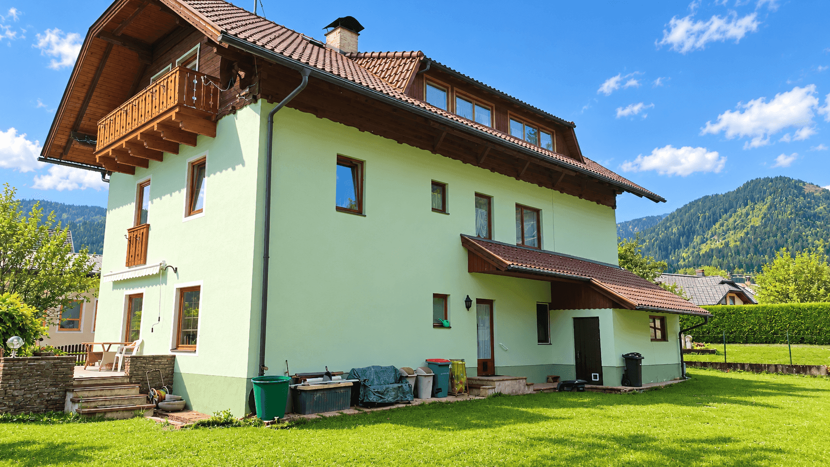 Rückansicht eines Hauses mit großem Garten und Bergblick unter strahlend blauem Himmel.