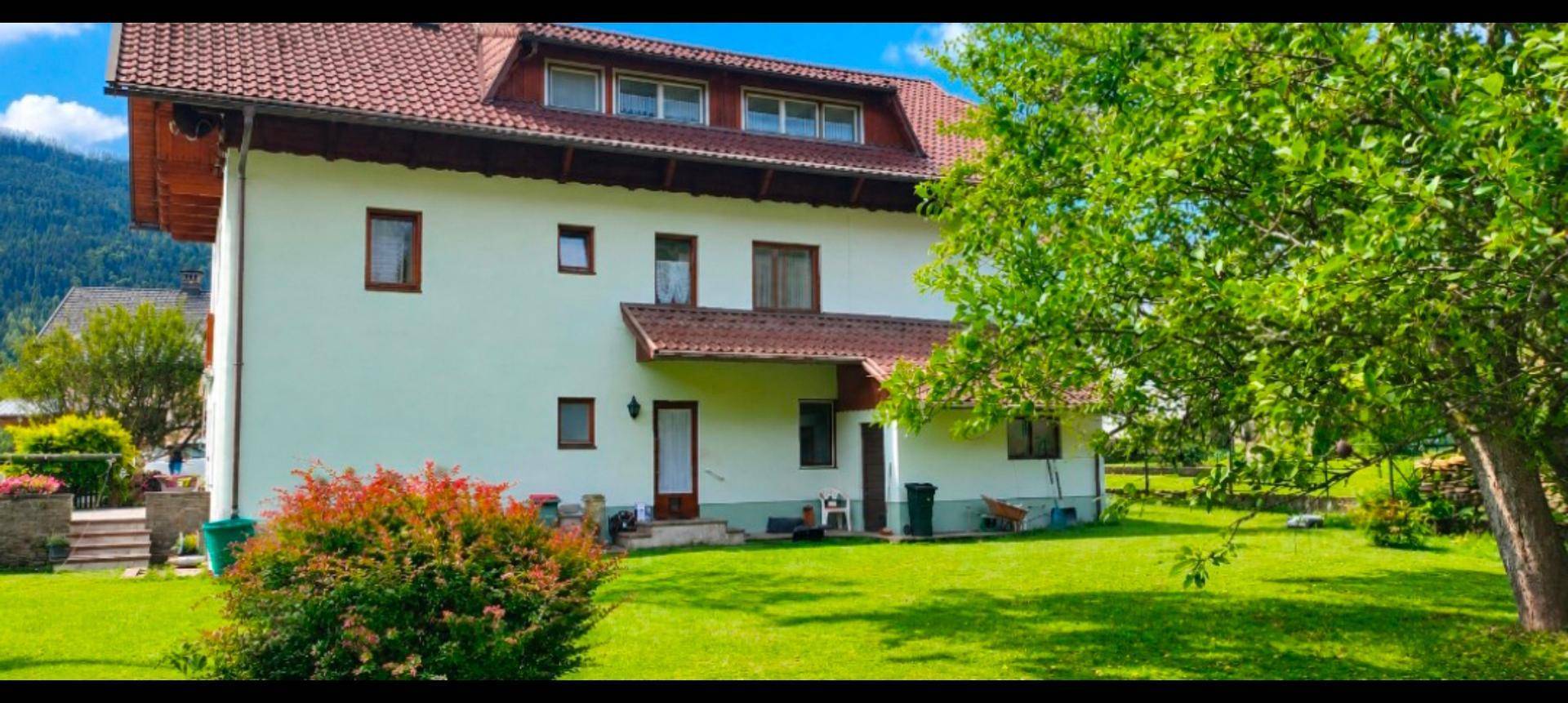 Rückseite des Hauses mit großem, gepflegtem Rasen und Bäumen im Hintergrund.