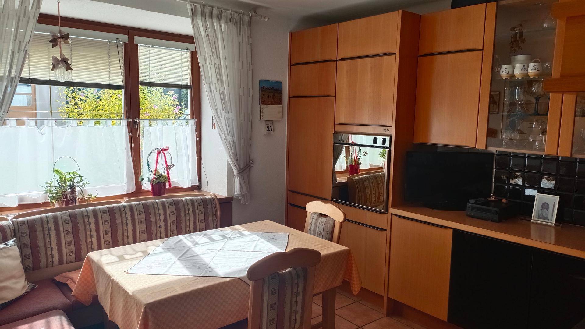 Gemütliche Wohnküche mit Holzeinbauten, Esstisch und Fenster mit Blick ins Grüne.