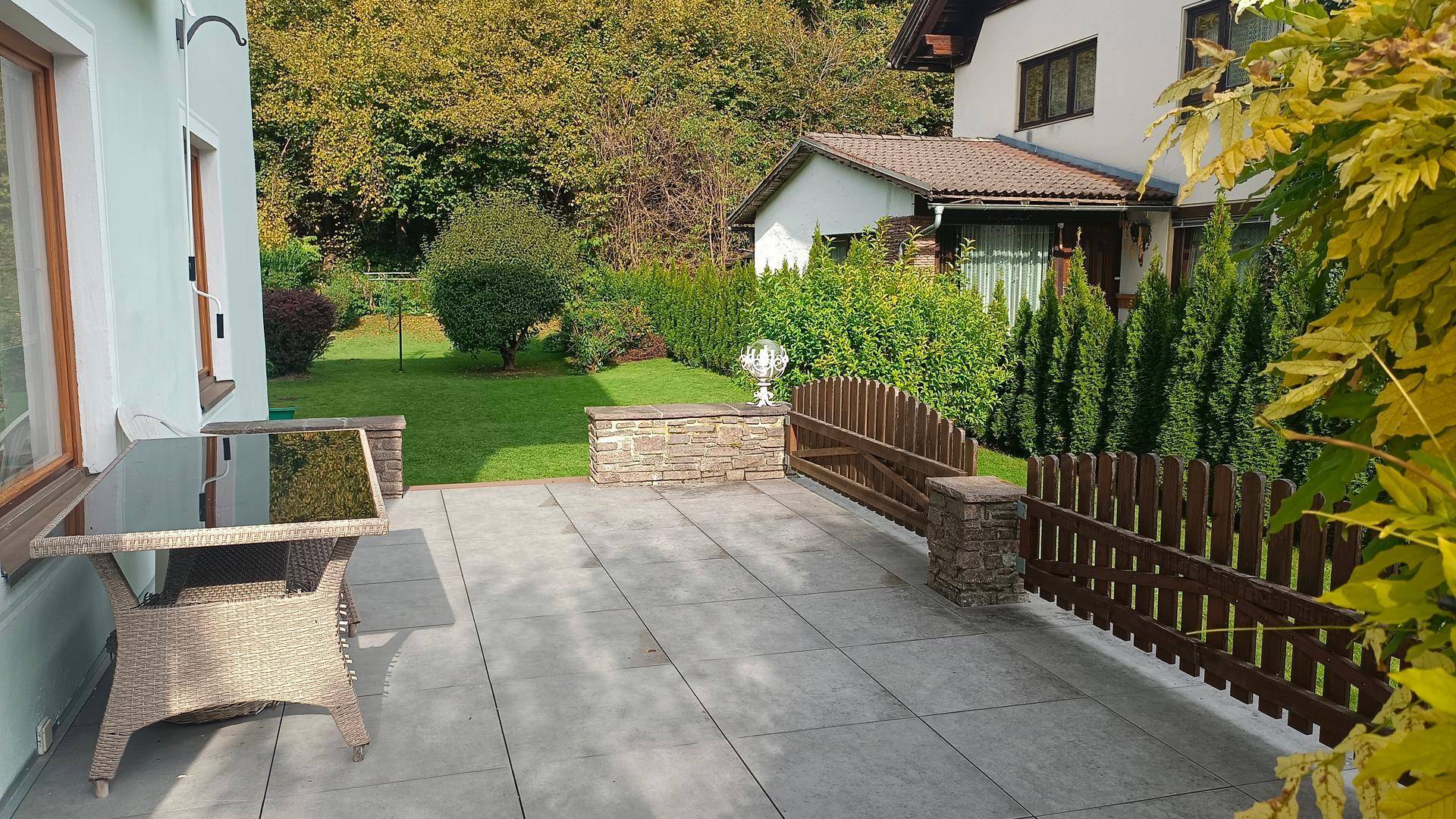 Gepflasterte Terrasse mit Gartenmöbeln und Blick auf den grünen Garten und bewaldete Hügel.