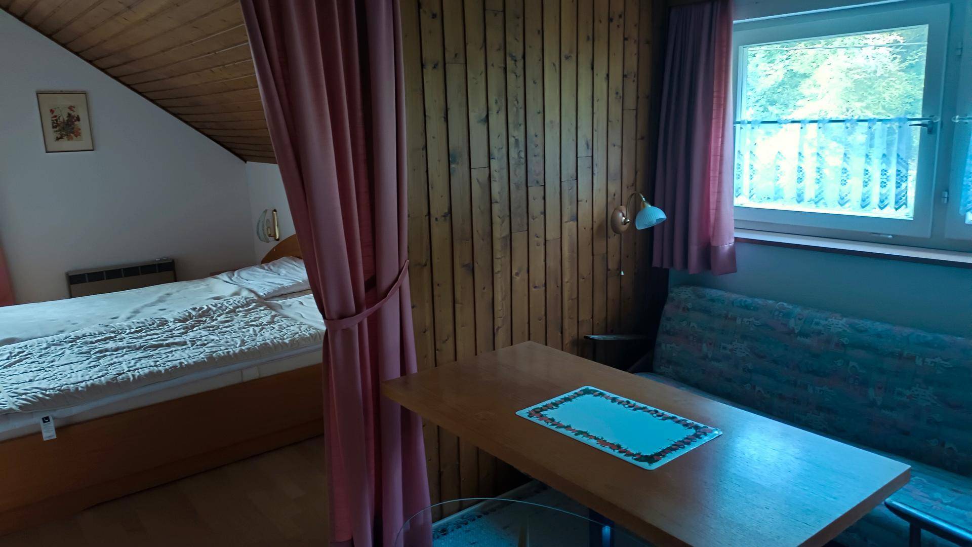 Gemütliches Schlafzimmer im Dachgeschoss mit Holzwänden, schrägen Decken und einem kleinen Essbereich.