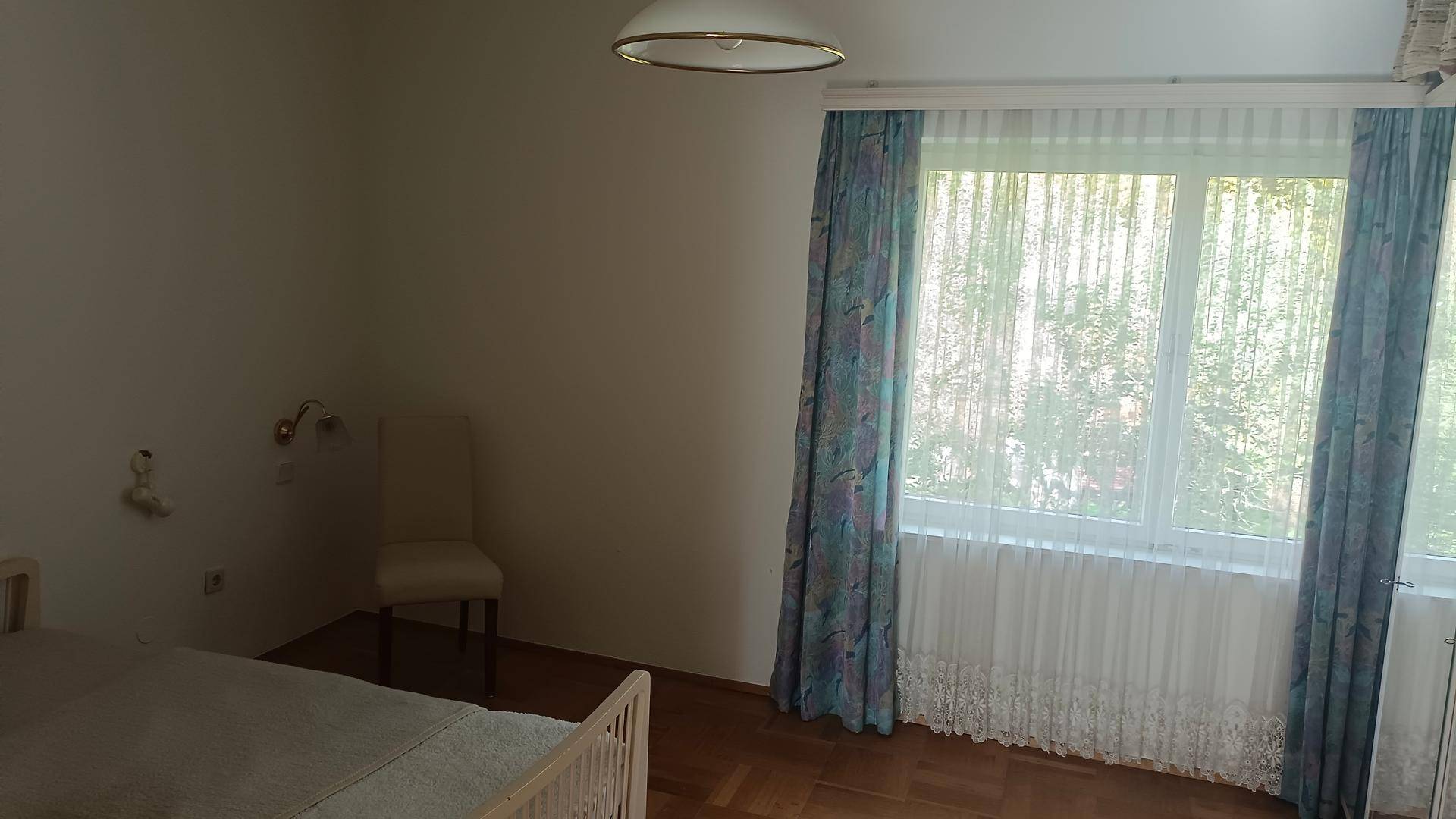 Helles Schlafzimmer mit Parkettboden und großem Fenster mit blauen Vorhängen.