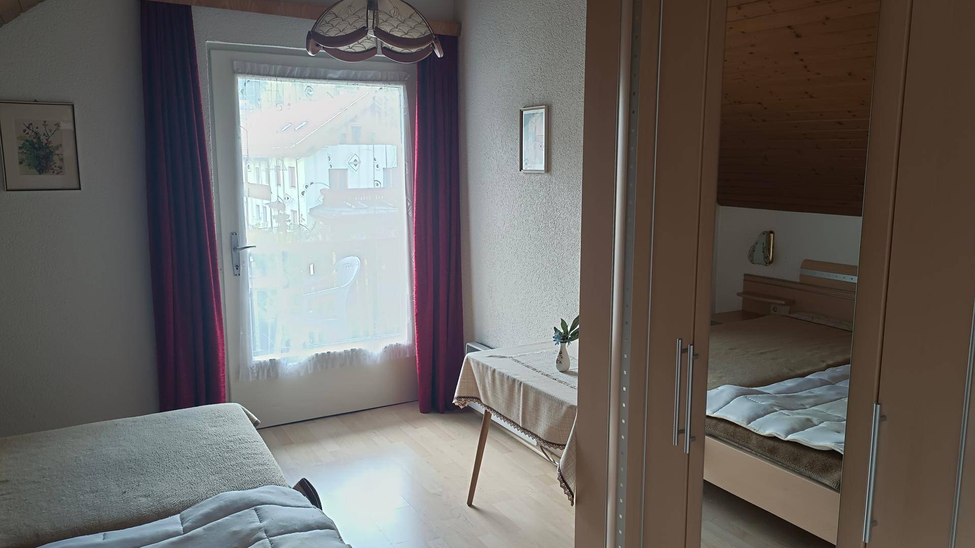 Schlafzimmer mit Einzelbett, Spiegelschrank und Zugang zu einem Balkon oder Terrasse.