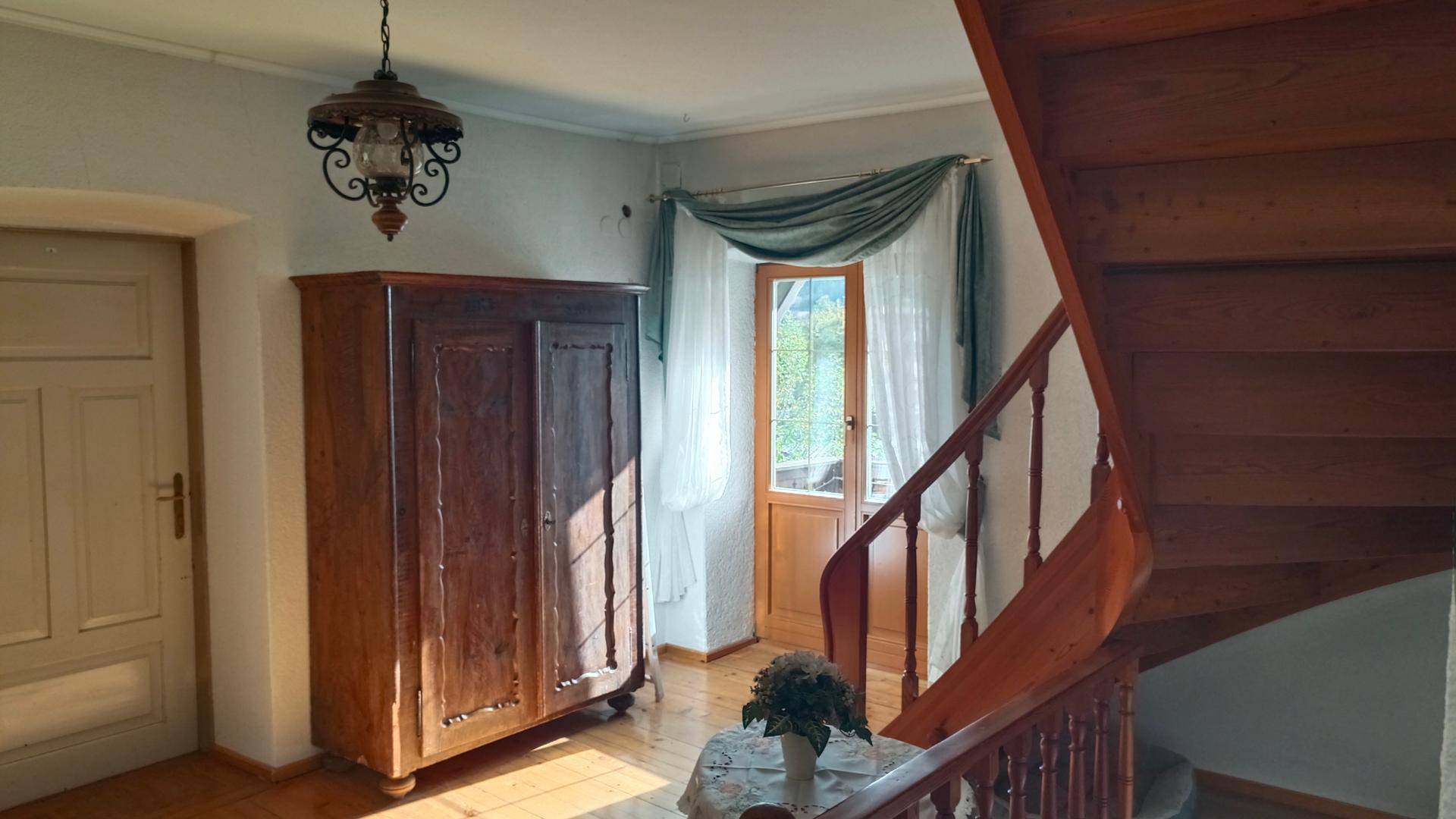 Flur mit Holztreppe, antiker Kommode und Fenster mit Blick nach draußen.