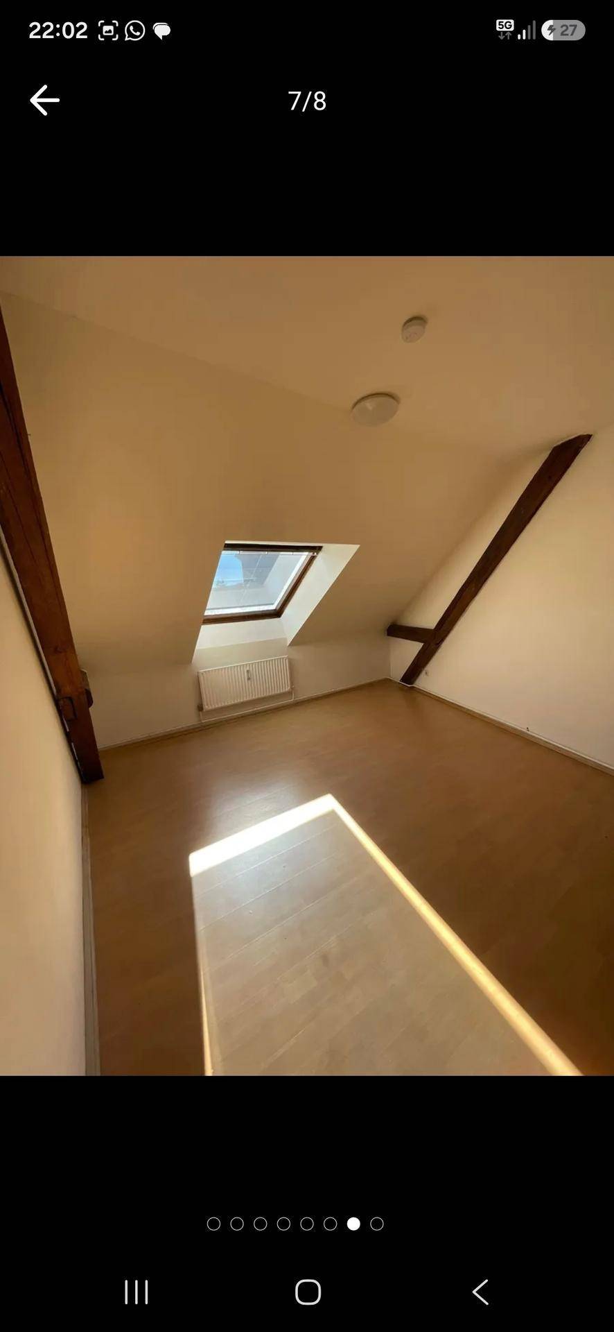 Heller Dachgeschossraum mit sichtbaren Holzbalken, Holzfußboden und einem Dachfenster, das viel Licht spendet.