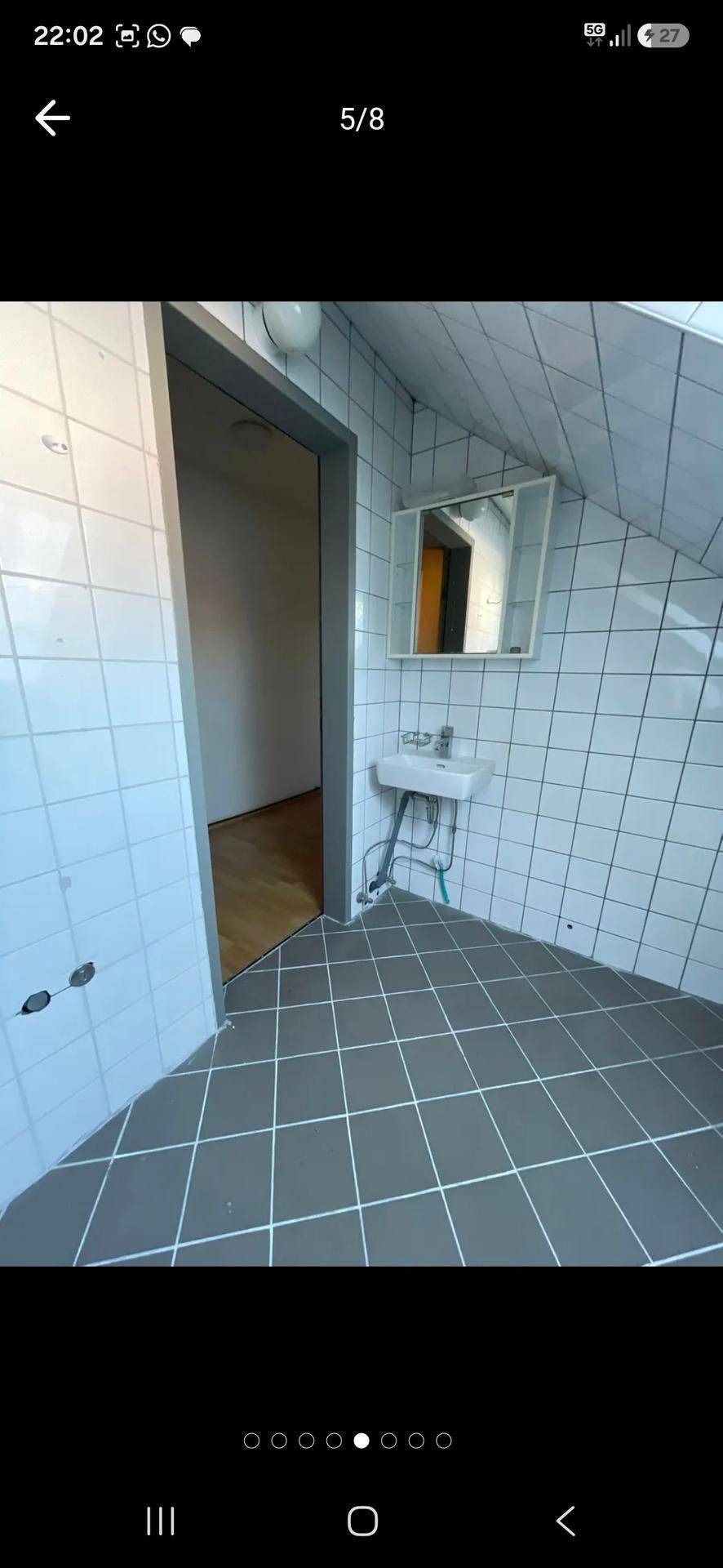 Kleiner gefliester Badbereich im Dachgeschoss mit Waschbecken, Spiegel und Zugang zu einem weiteren Raum.