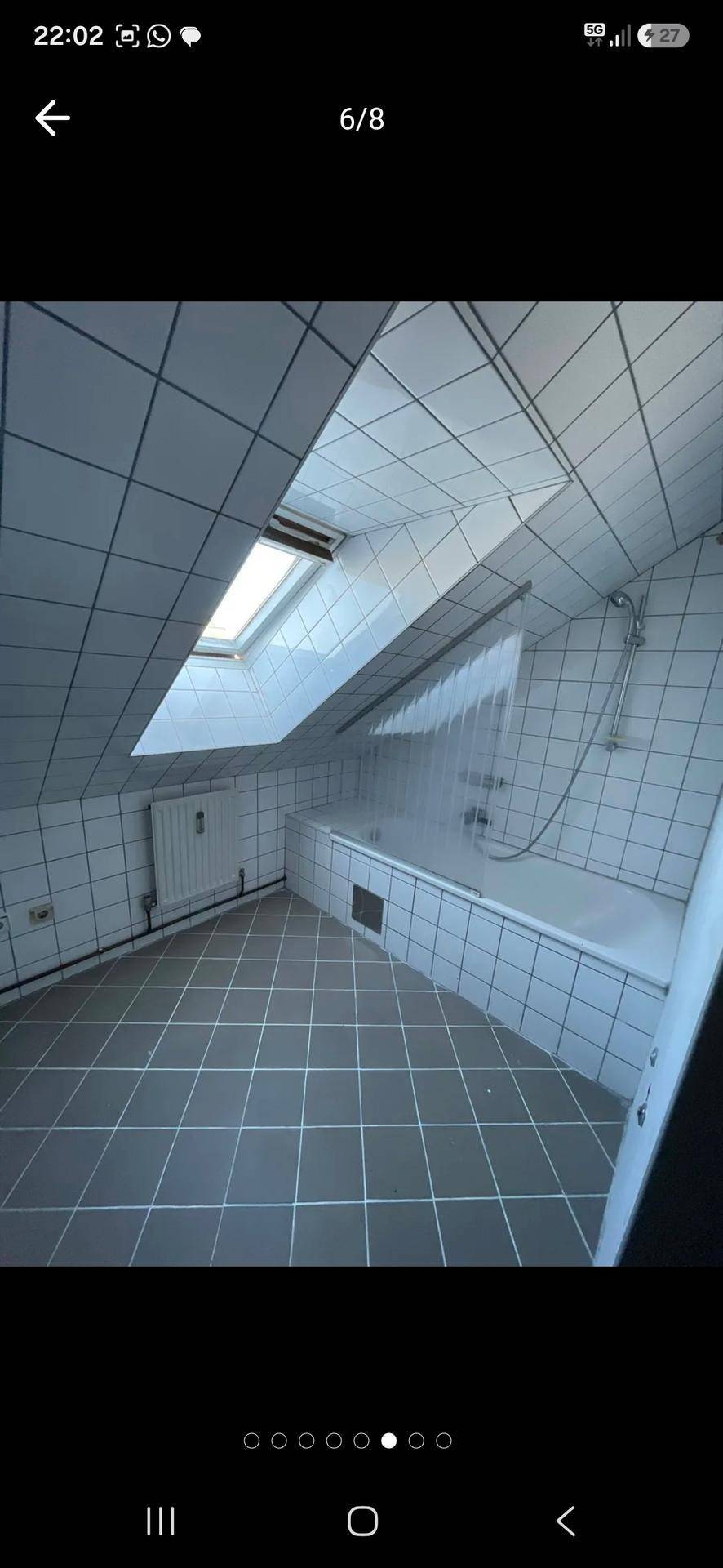 Gefliestes Dachgeschossbad mit Badewanne, Duschvorrichtung und einem Dachfenster, das den Raum erhellt.