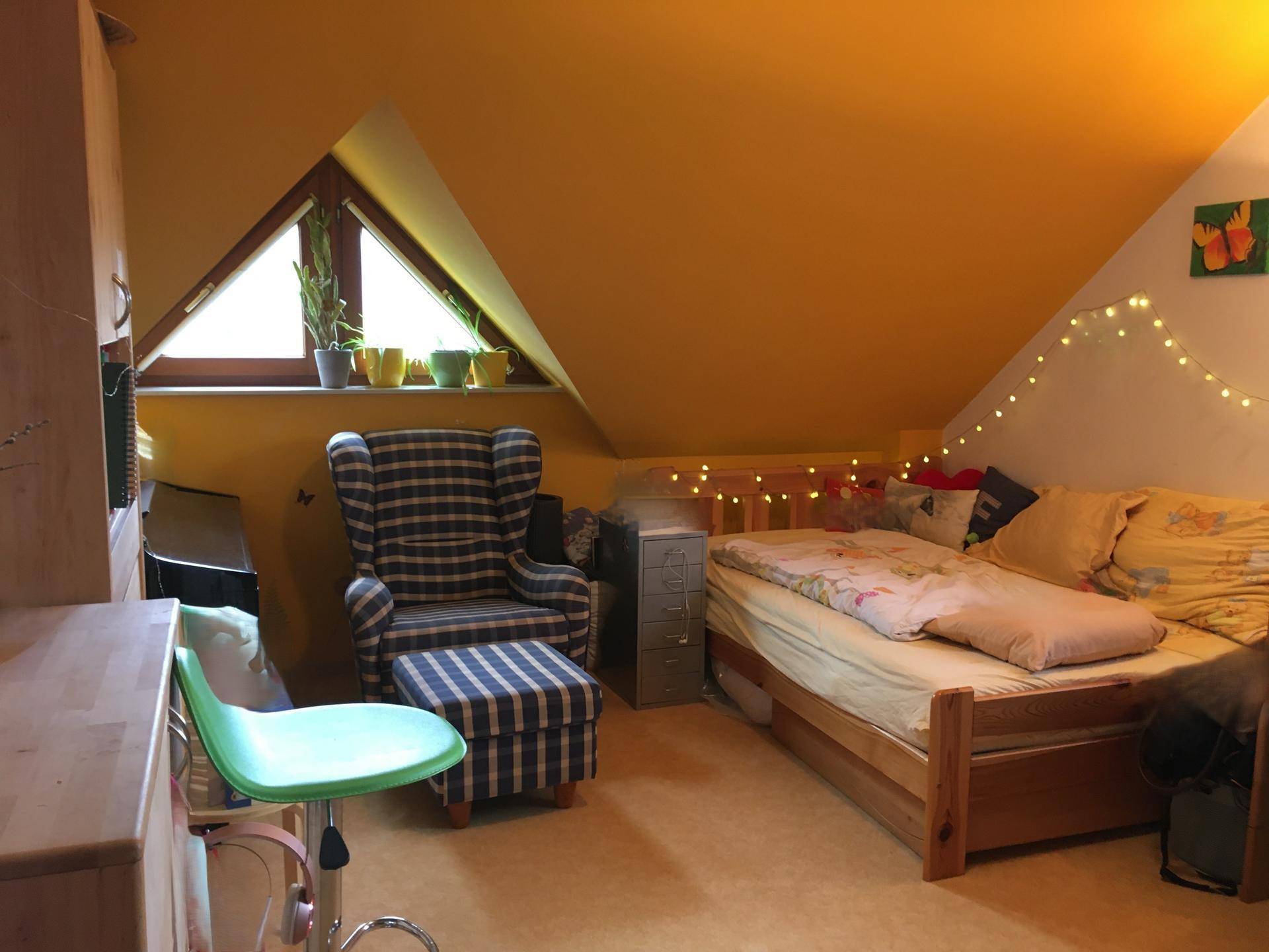Gemütliches Schlafzimmer mit Dachschräge, Fenster, Einzelbett und gelben Wänden.