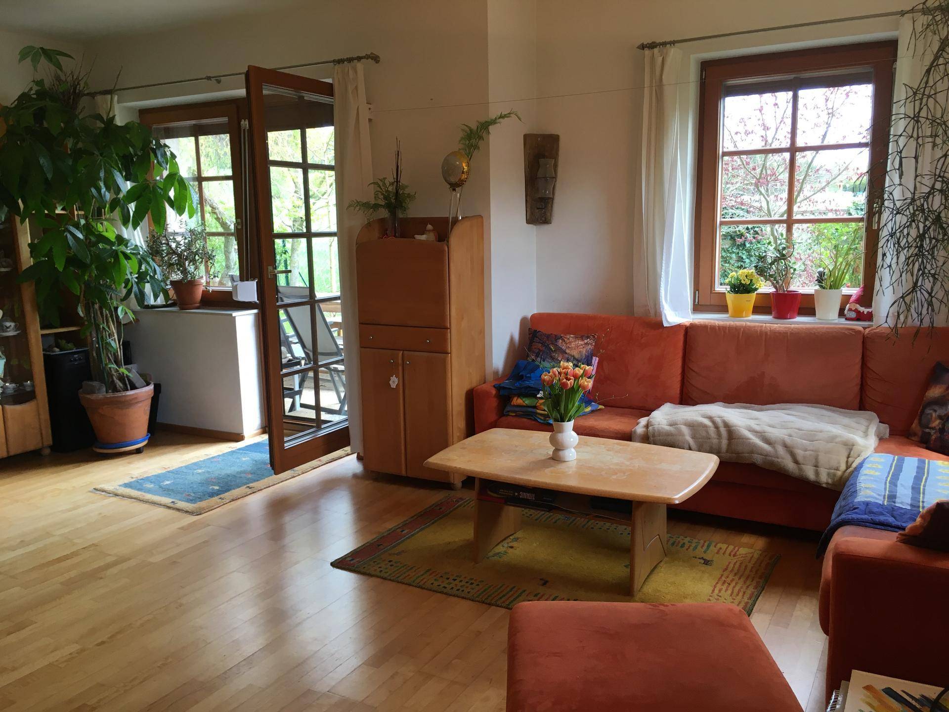 Helles Wohnzimmer mit orangefarbenem Sofa, Holzboden und Zugang zu einem Außenbereich.