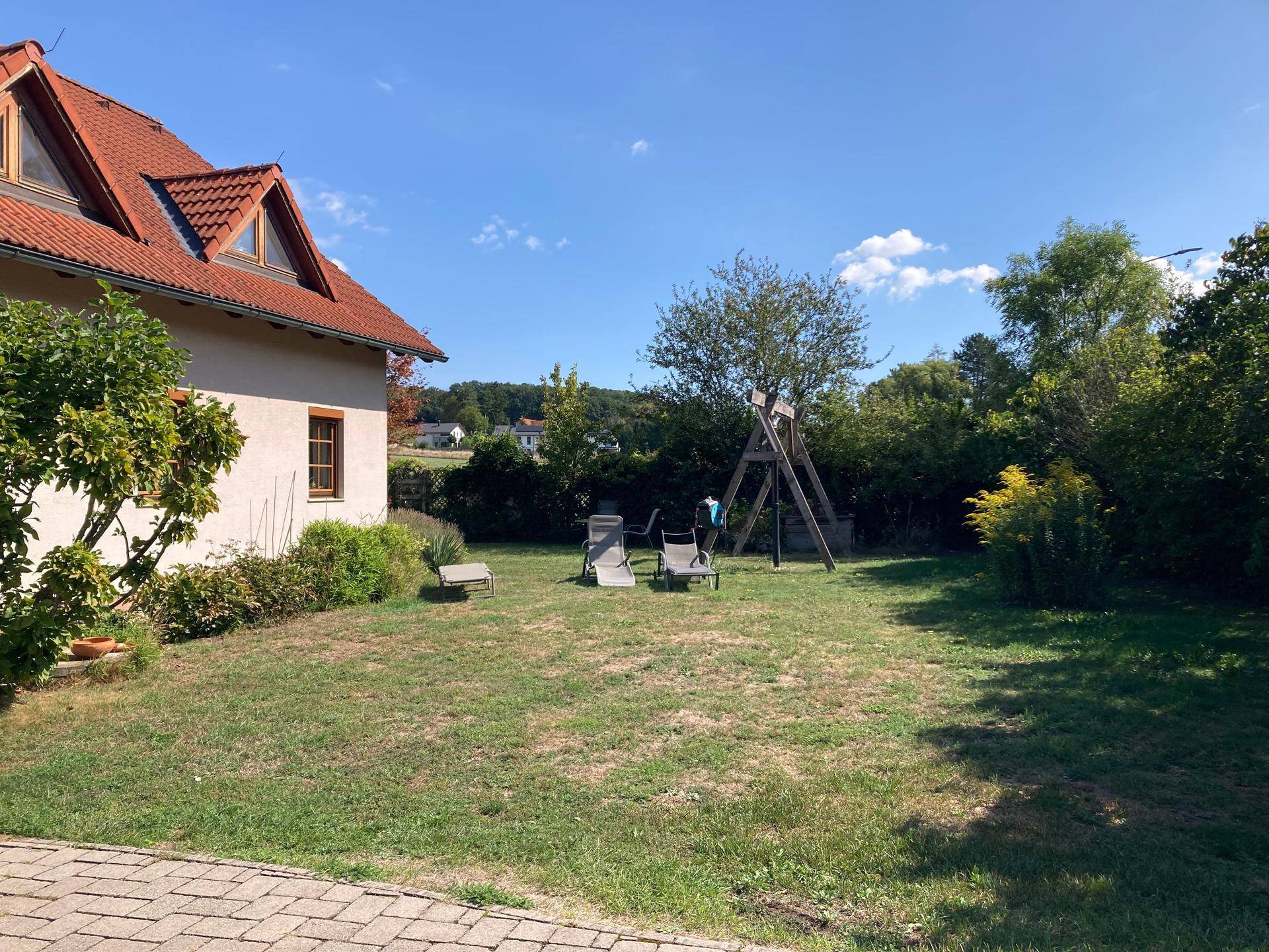 Weitläufiger Garten mit Rasenfläche, Schaukel und Blick auf die Nachbarschaft sowie die grüne Umgebung.