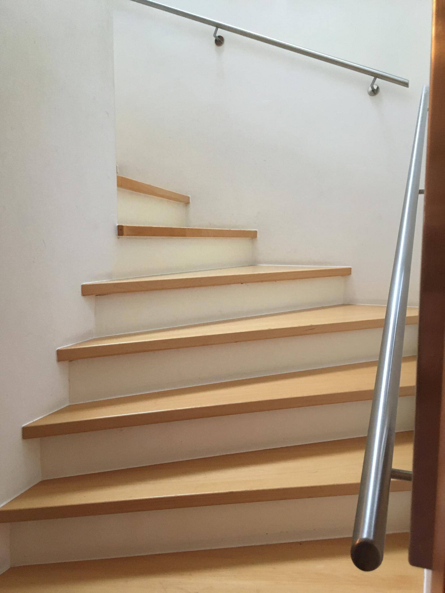 Moderne Holztreppe mit elegantem Metallgeländer, die die Stockwerke verbindet.