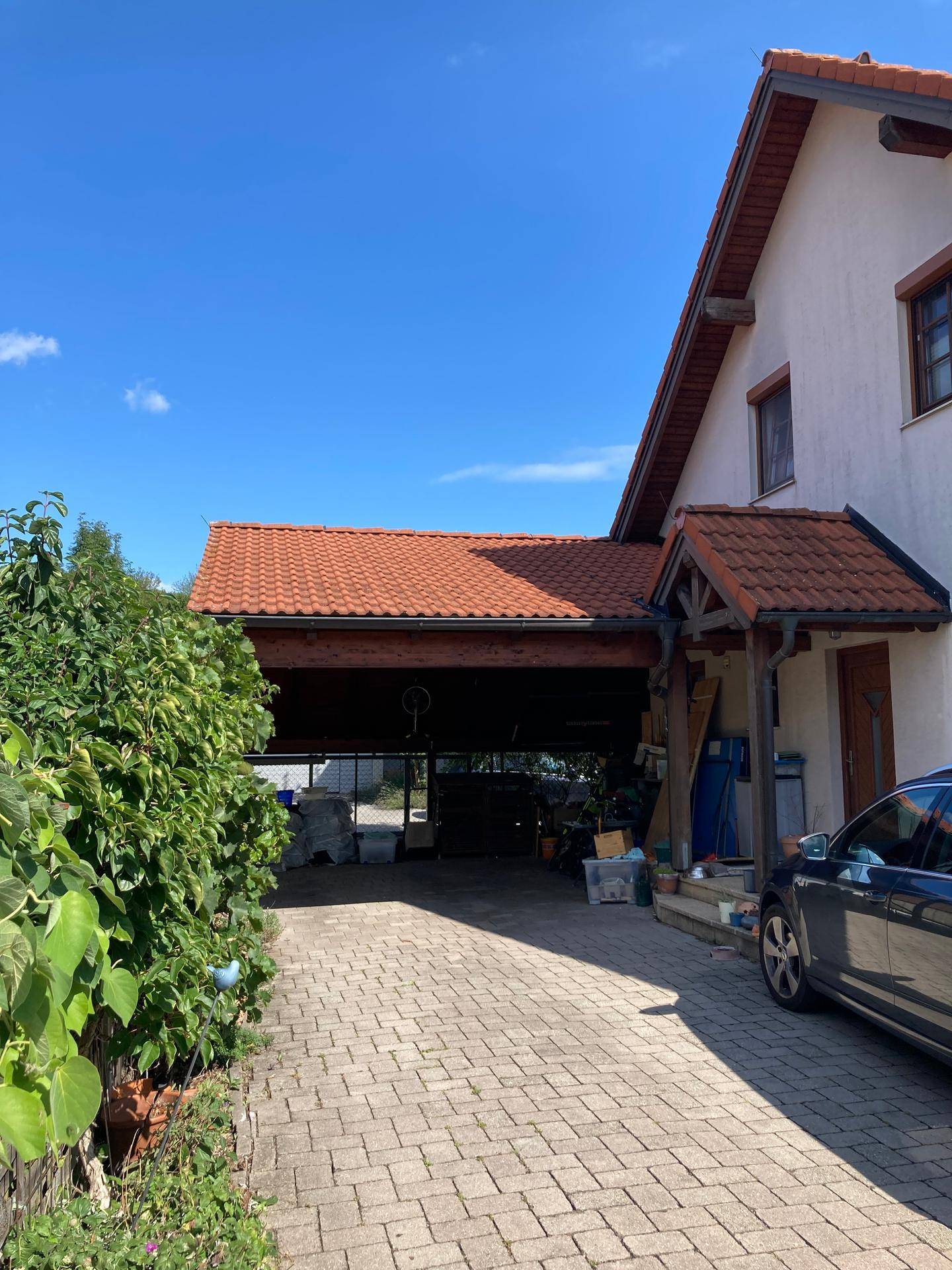 Gepflasterte Einfahrt führt zu einem überdachten Carport neben dem Haus mit rotem Ziegeldach.