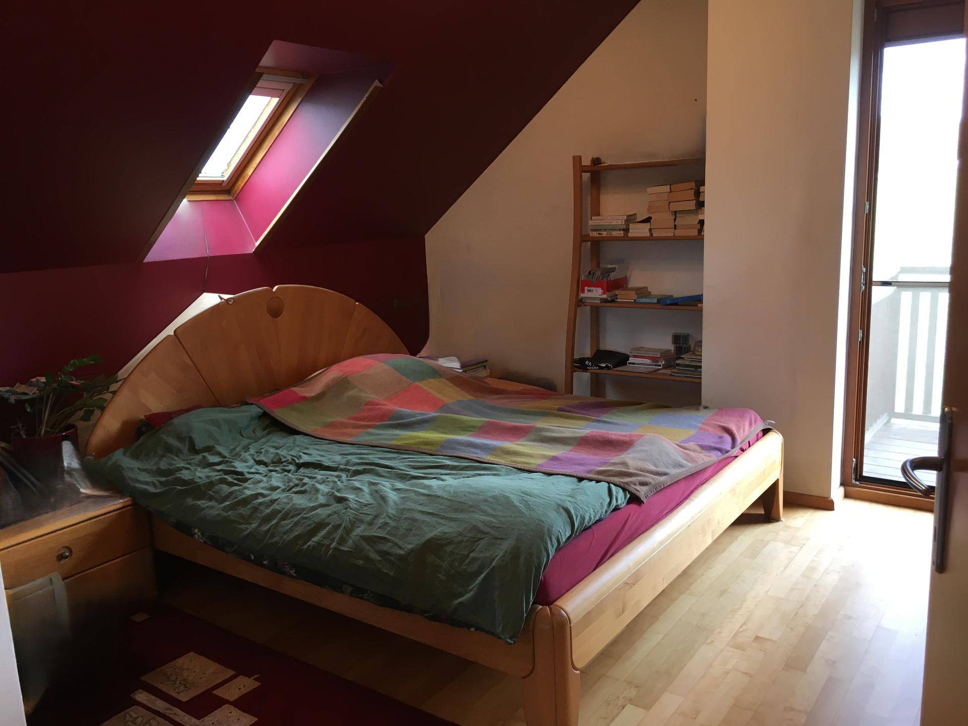 Schlafzimmer mit Holzbett, Dachschräge, Dachfenster und Zugang zu einem Balkon.