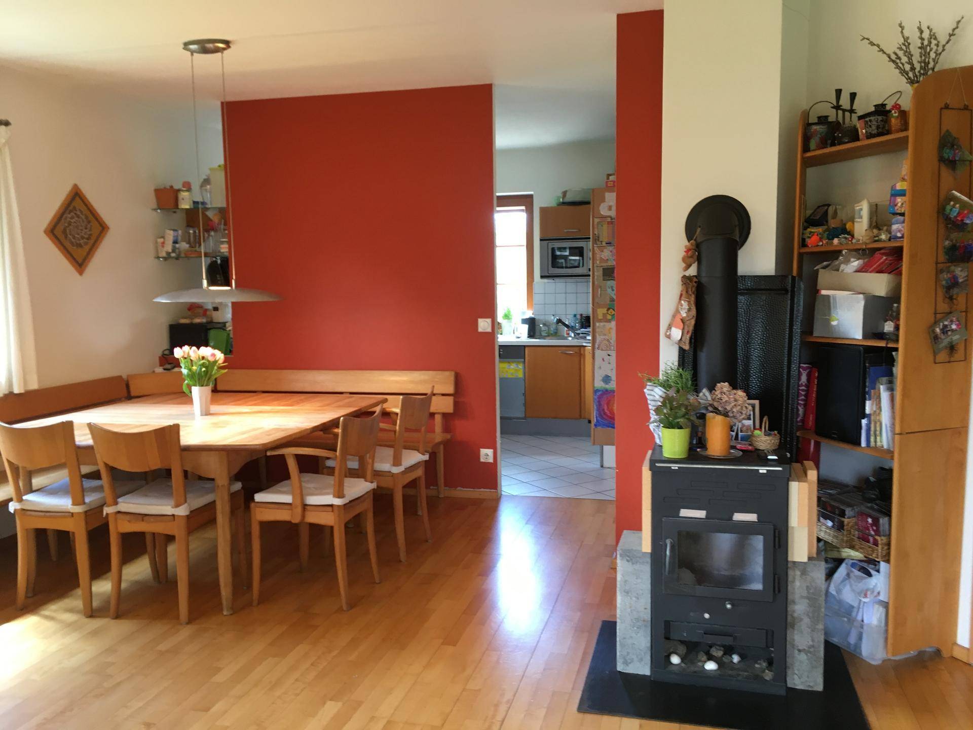 Essbereich mit Kaminofen und roter Akzentwand, angrenzend an die Küche mit Holzboden.