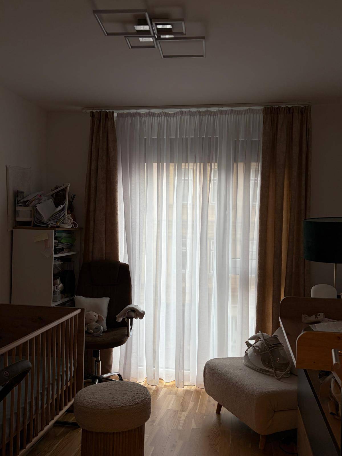 Gemütliches Schlafzimmer mit Kinderbett, Vorhängen und einem großen Fenster, das Tageslicht hereinlässt.