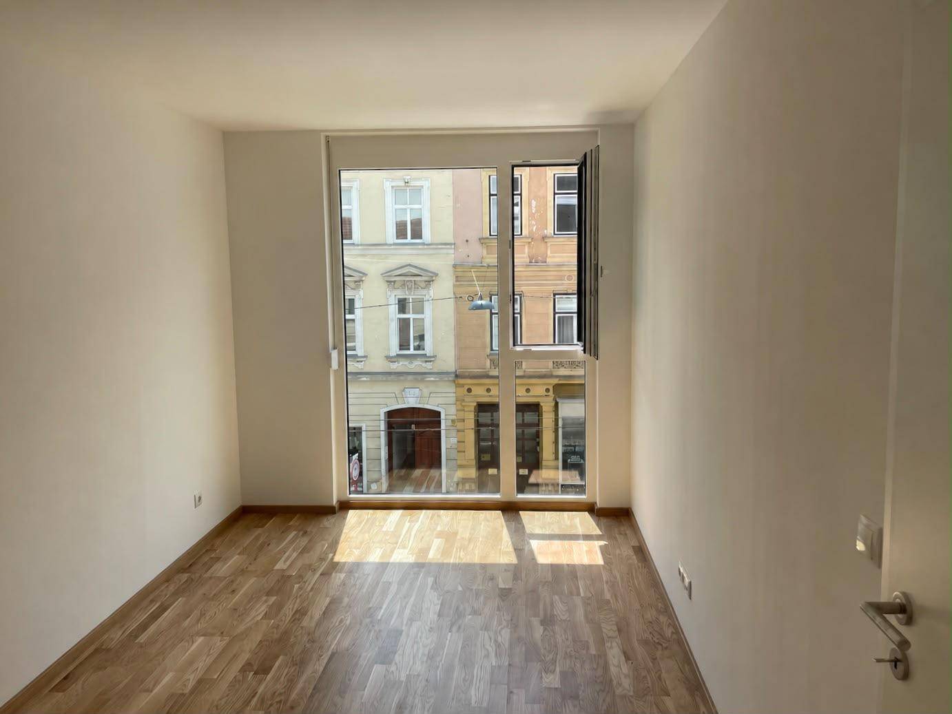 Heller Raum mit Holzboden und großem Fenster, das einen Blick auf die belebte Straße bietet.