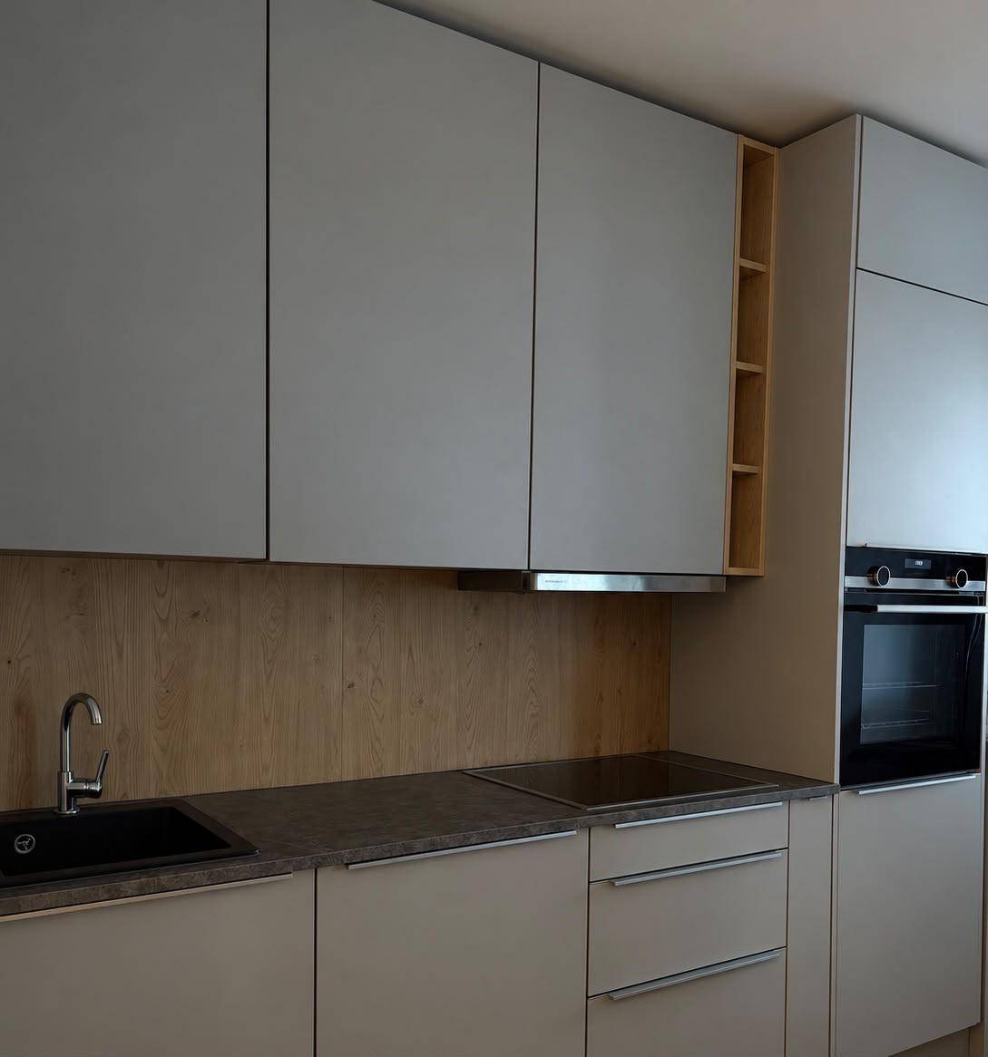 Detailansicht der modernen Küche mit Spüle, Induktionskochfeld, Backofen und Holzrückwand.