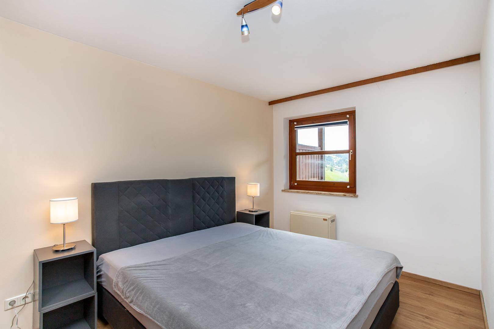 Schlafzimmer mit Doppelbett, Nachttischen und einem Fenster mit Blick ins Grüne.