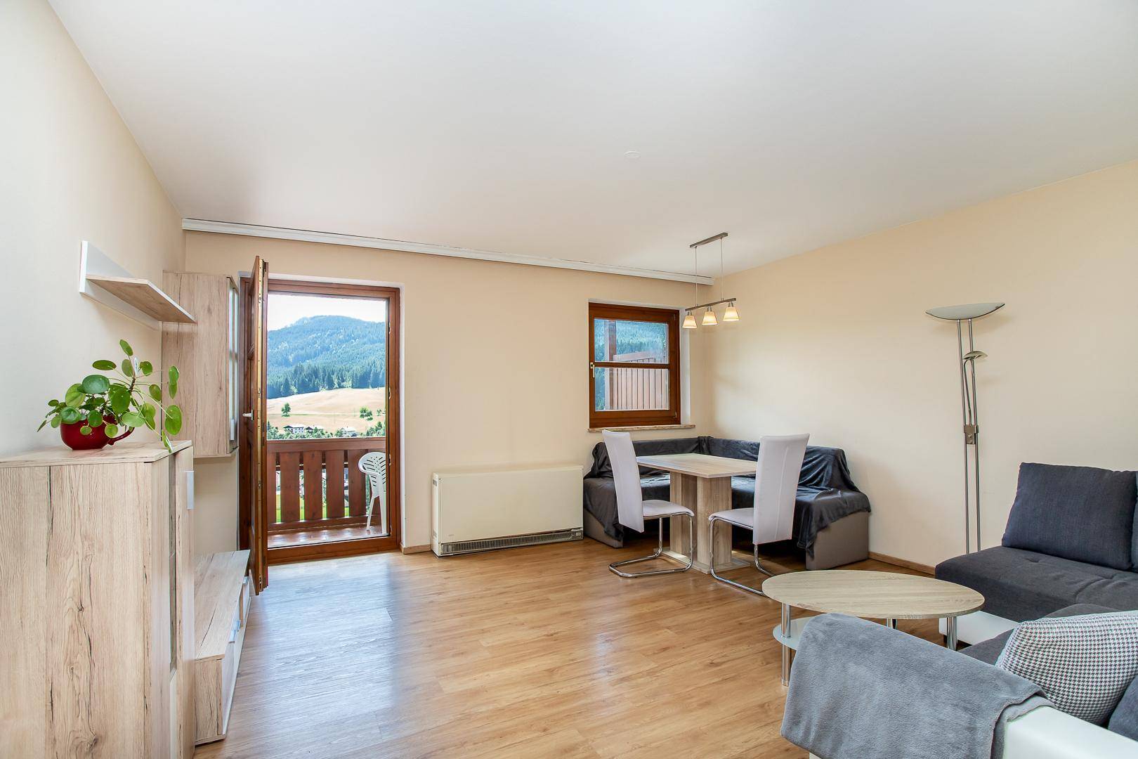 Heller Wohn- und Essbereich mit Holzboden und Zugang zu einem Balkon mit Bergblick.