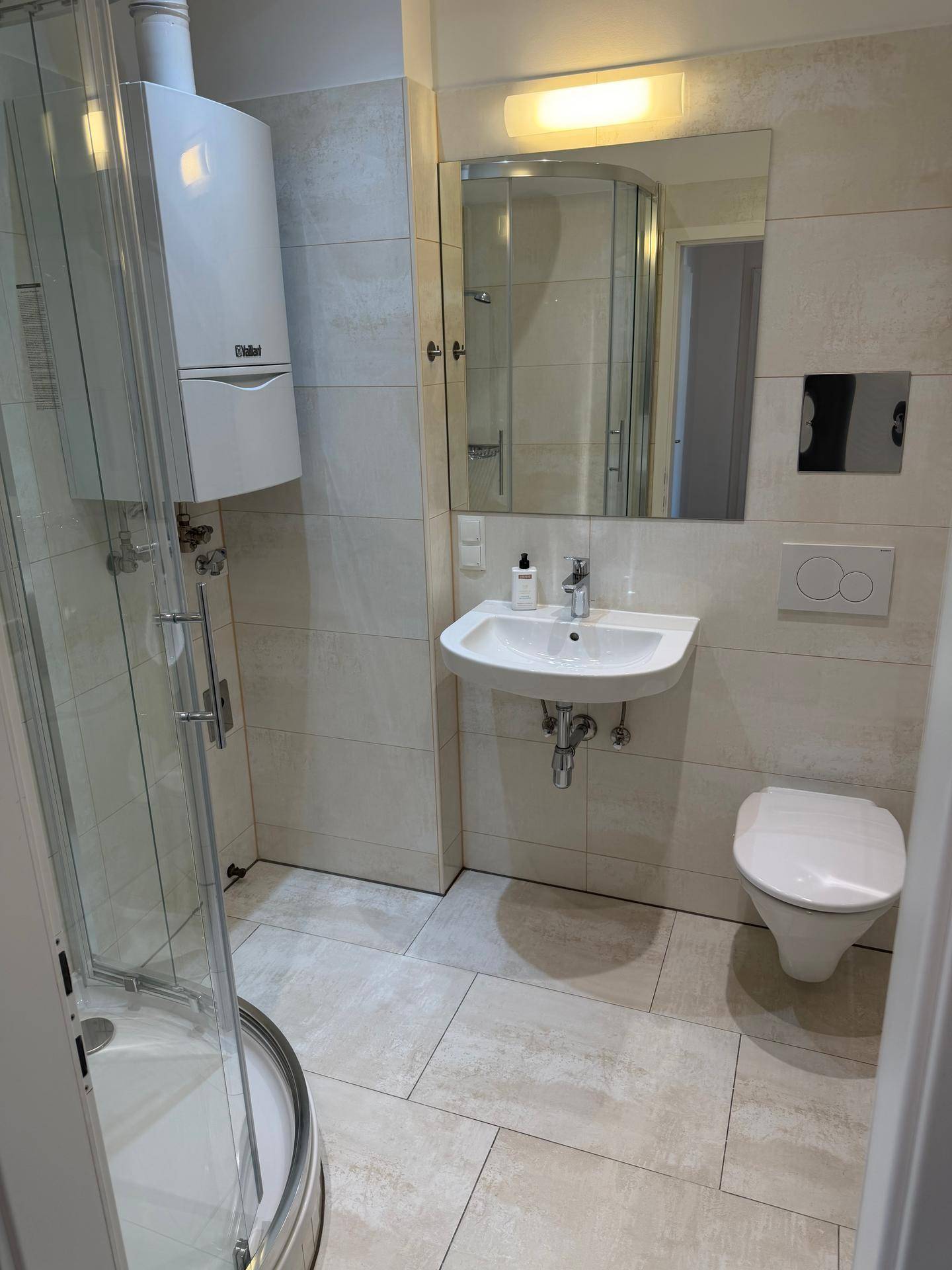 Helles Badezimmer mit Duschkabine, Waschbecken, Toilette und Wandheizung.