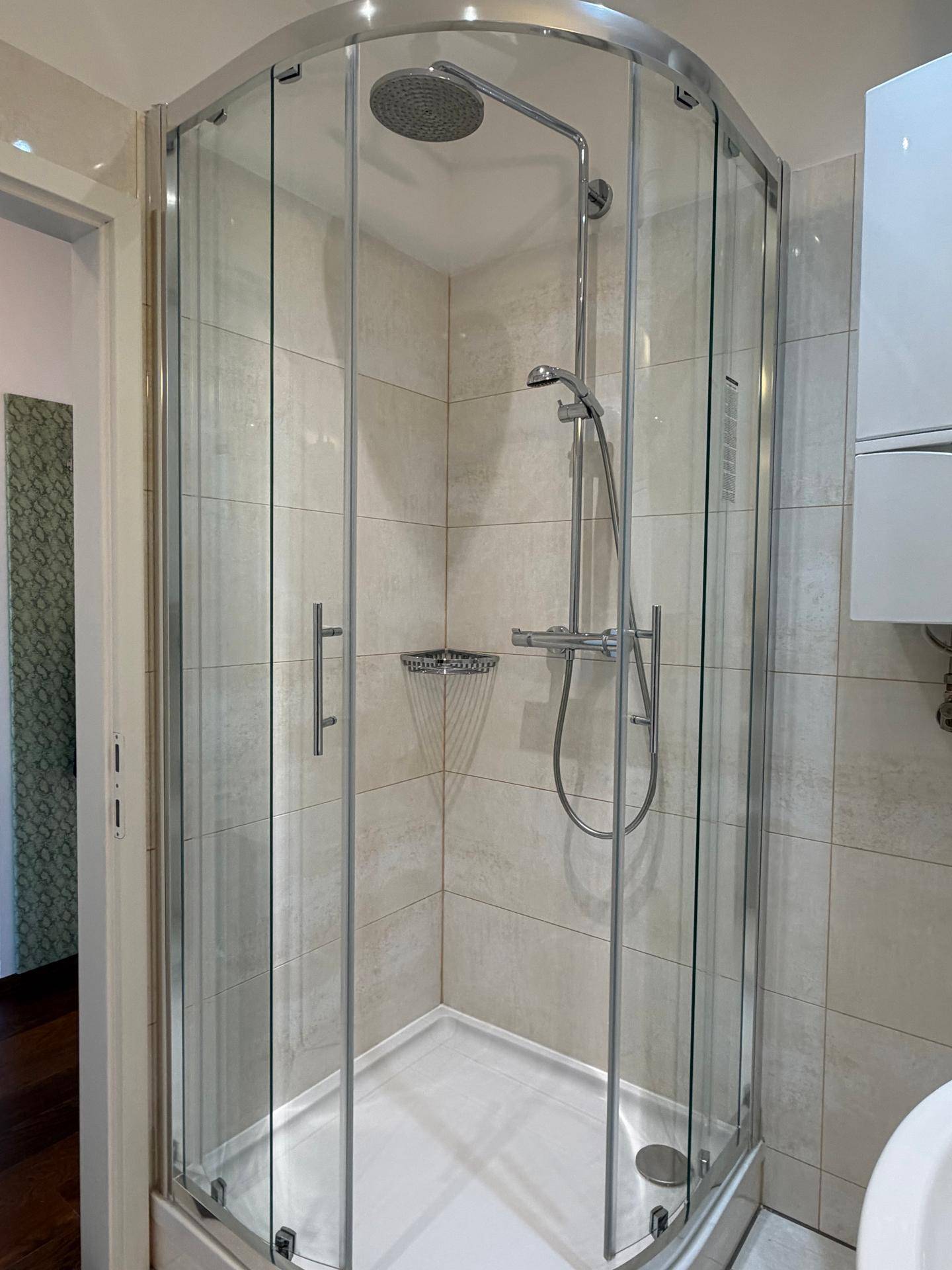 Moderne Eckduschkabine mit Glaswänden, Regendusche und hellen Fliesen.