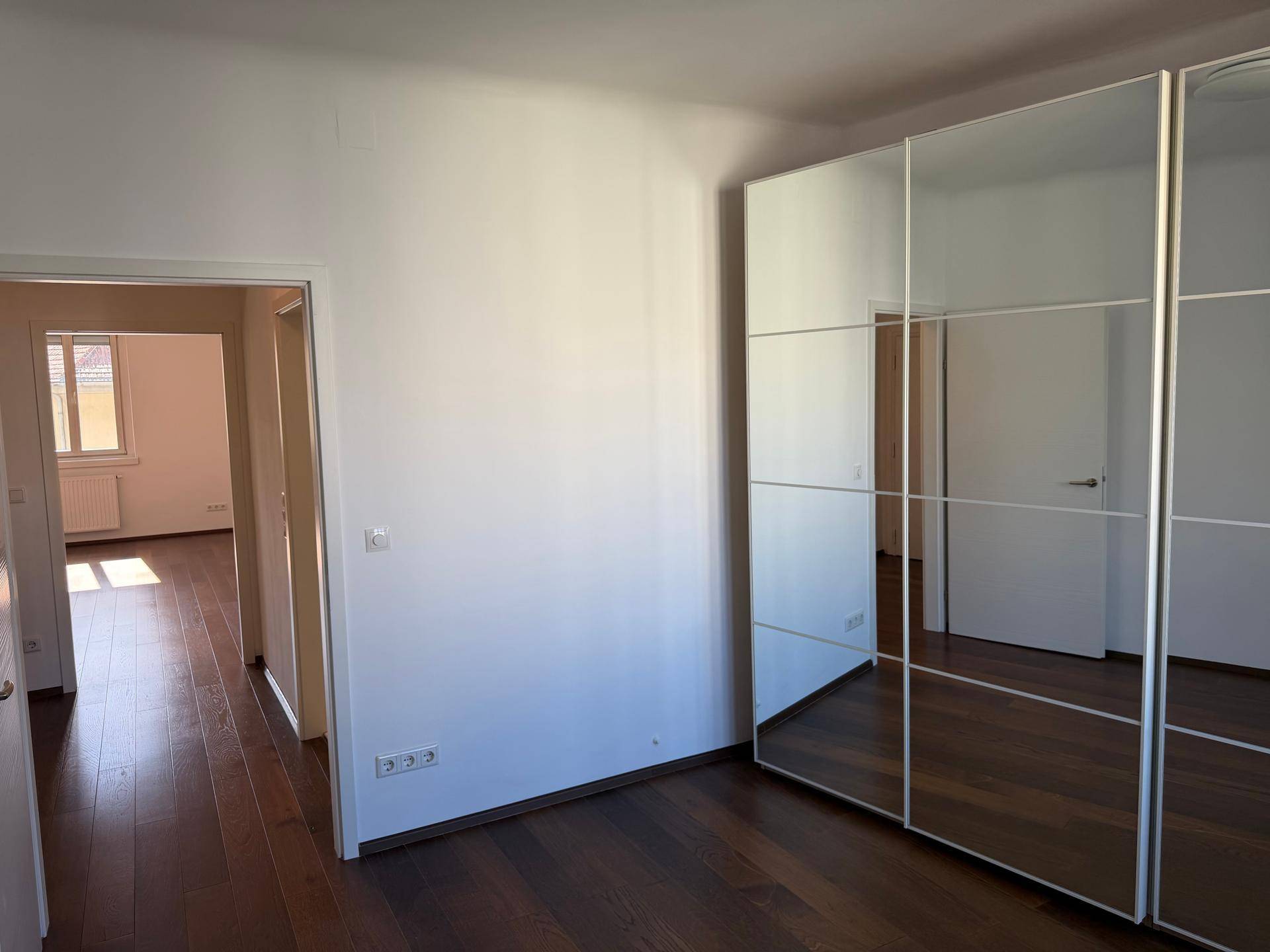 Geräumiges Schlafzimmer mit dunklem Parkettboden und einem großen Spiegelschrank.