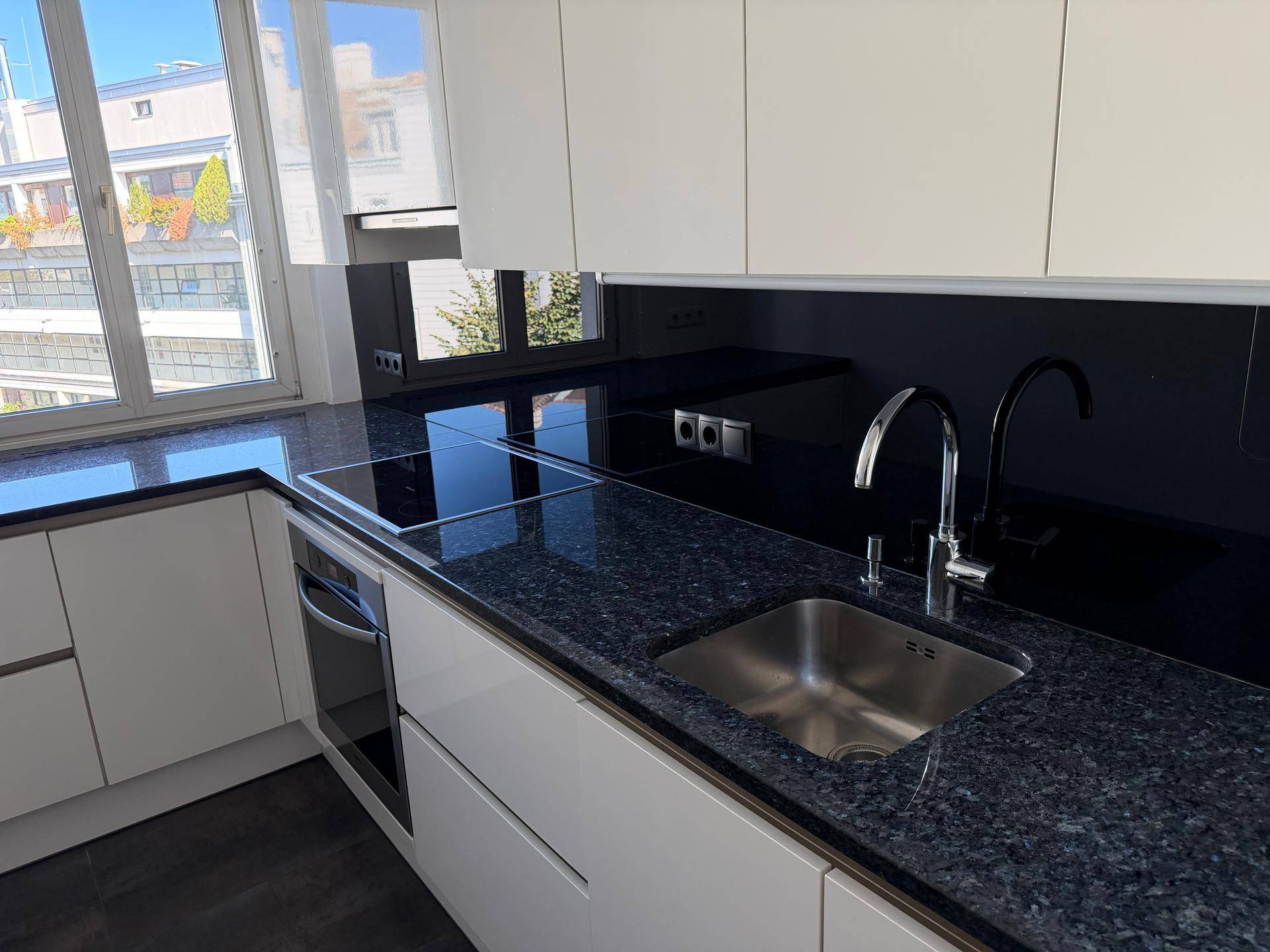 Moderne Küche mit dunkler Granitarbeitsplatte, Spüle, Induktionskochfeld und weißen Schränken.