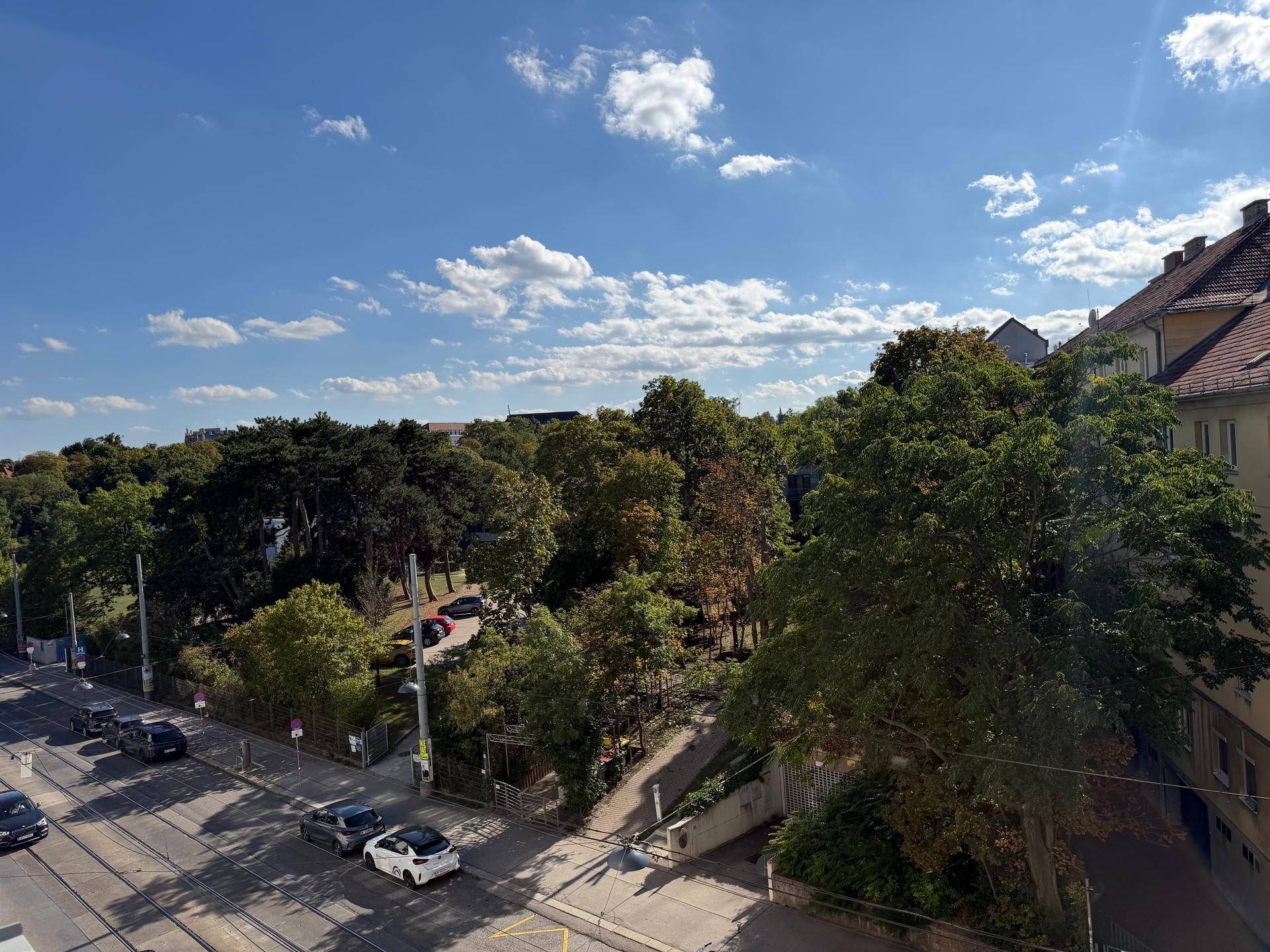 Weitläufiger Blick über eine grüne Parkanlage, eine belebte Straße und umliegende Gebäude.