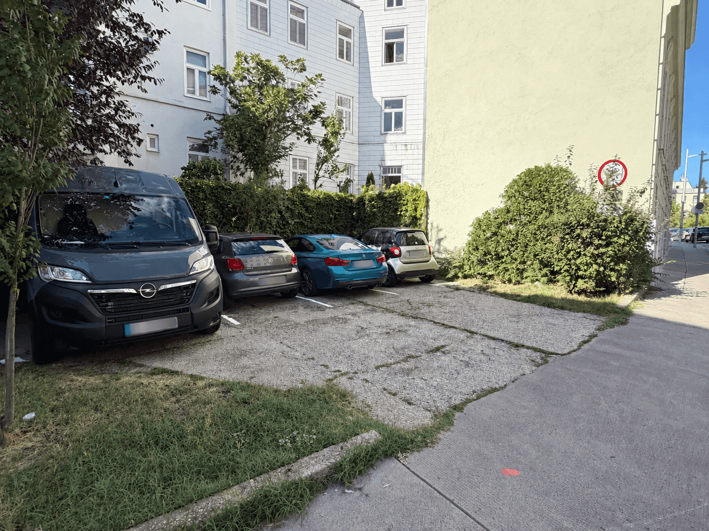 Außenparkplätze für mehrere Fahrzeuge neben einem Gebäude mit Grünflächen.