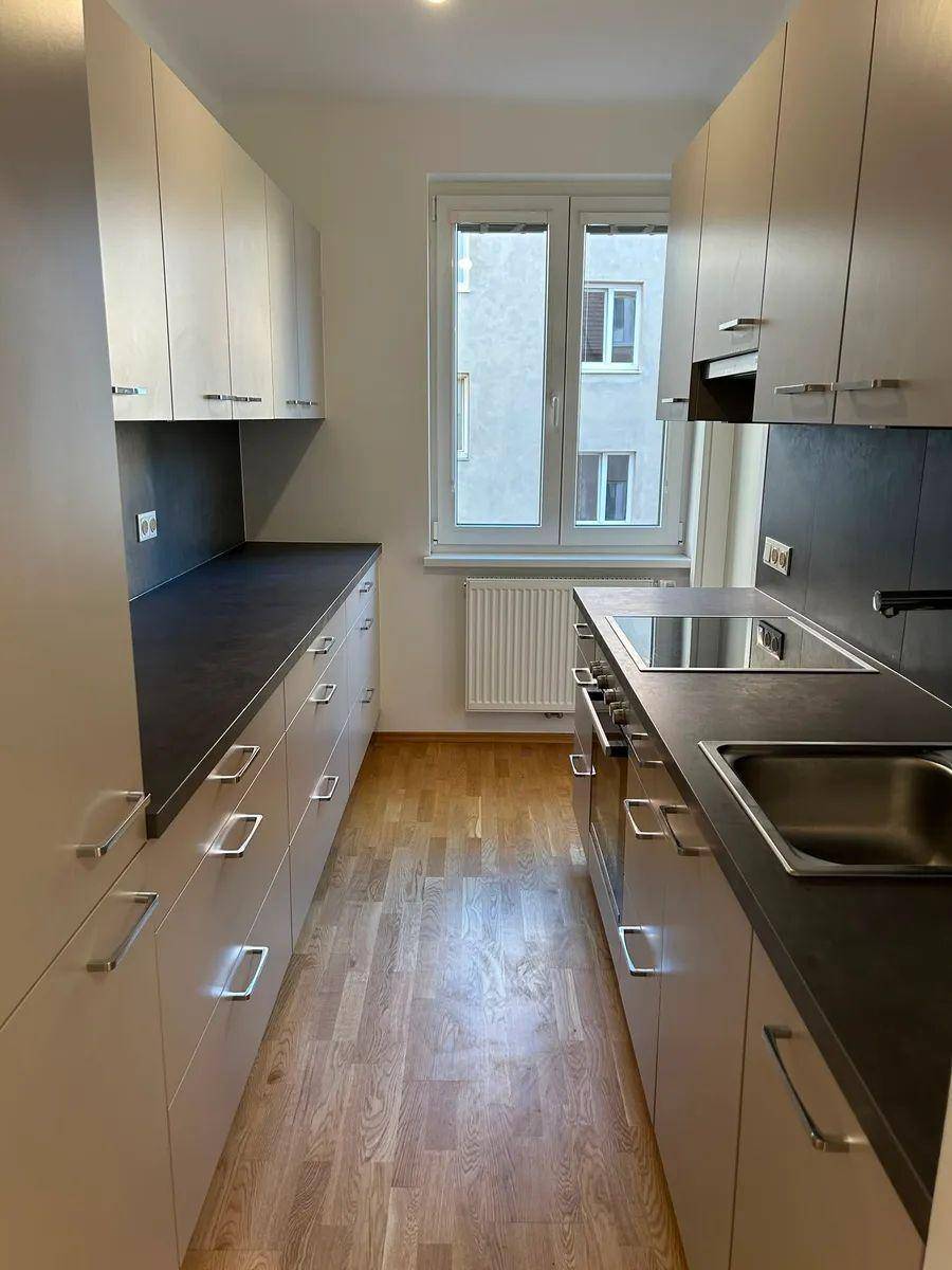 Funktionale Küche mit hellen Schränken, dunkler Arbeitsplatte und Fenster für natürliche Belichtung.